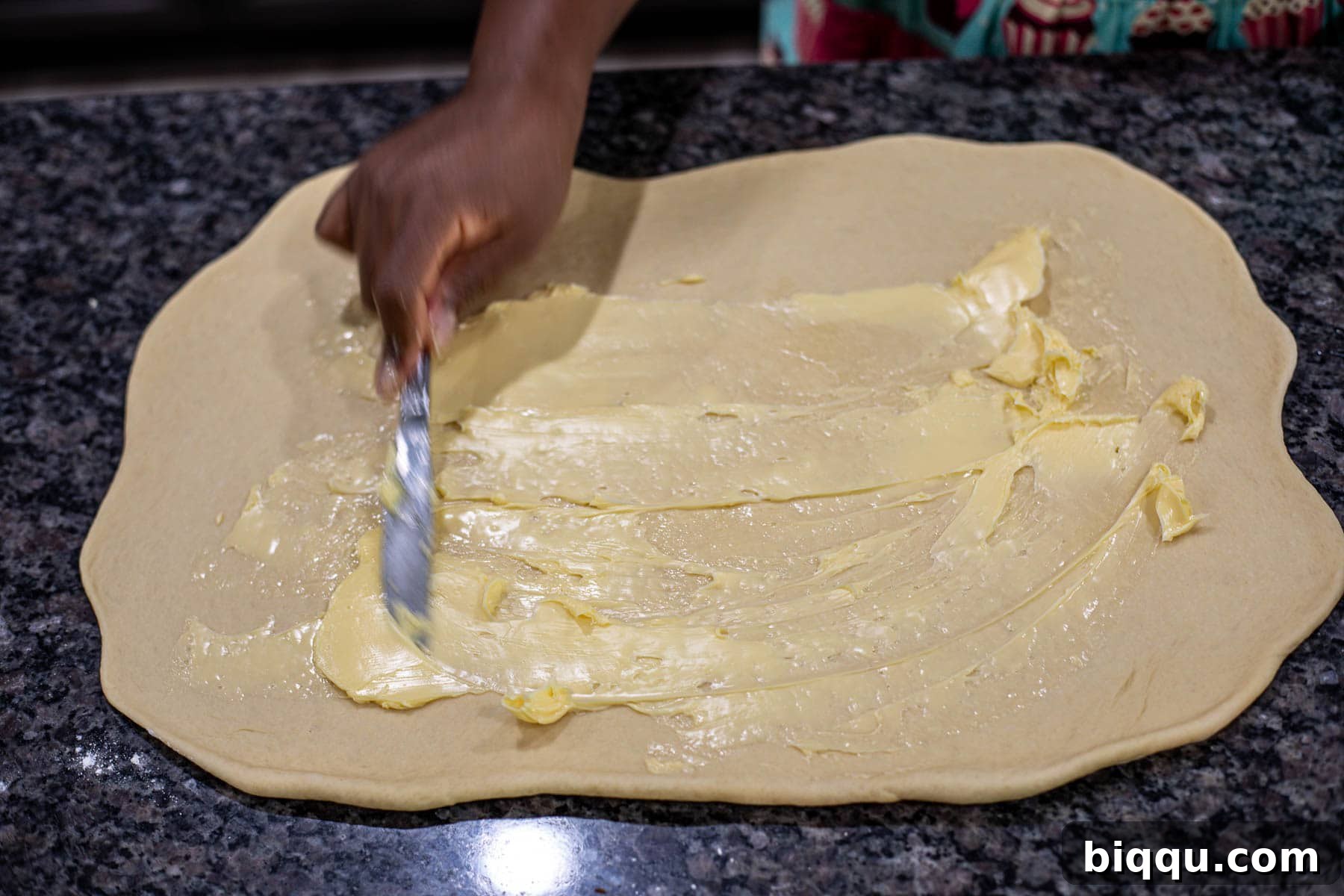 Hand spreading softened butter on rolled out dough.