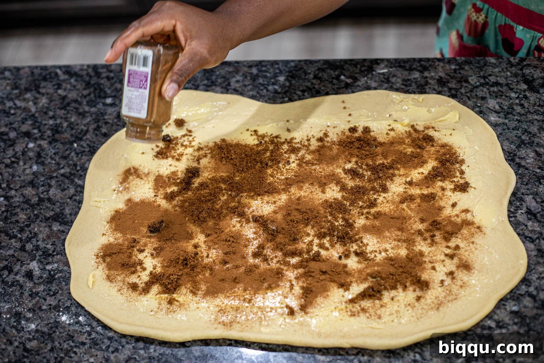 Hand sprinkling ground cinnamon over dough.