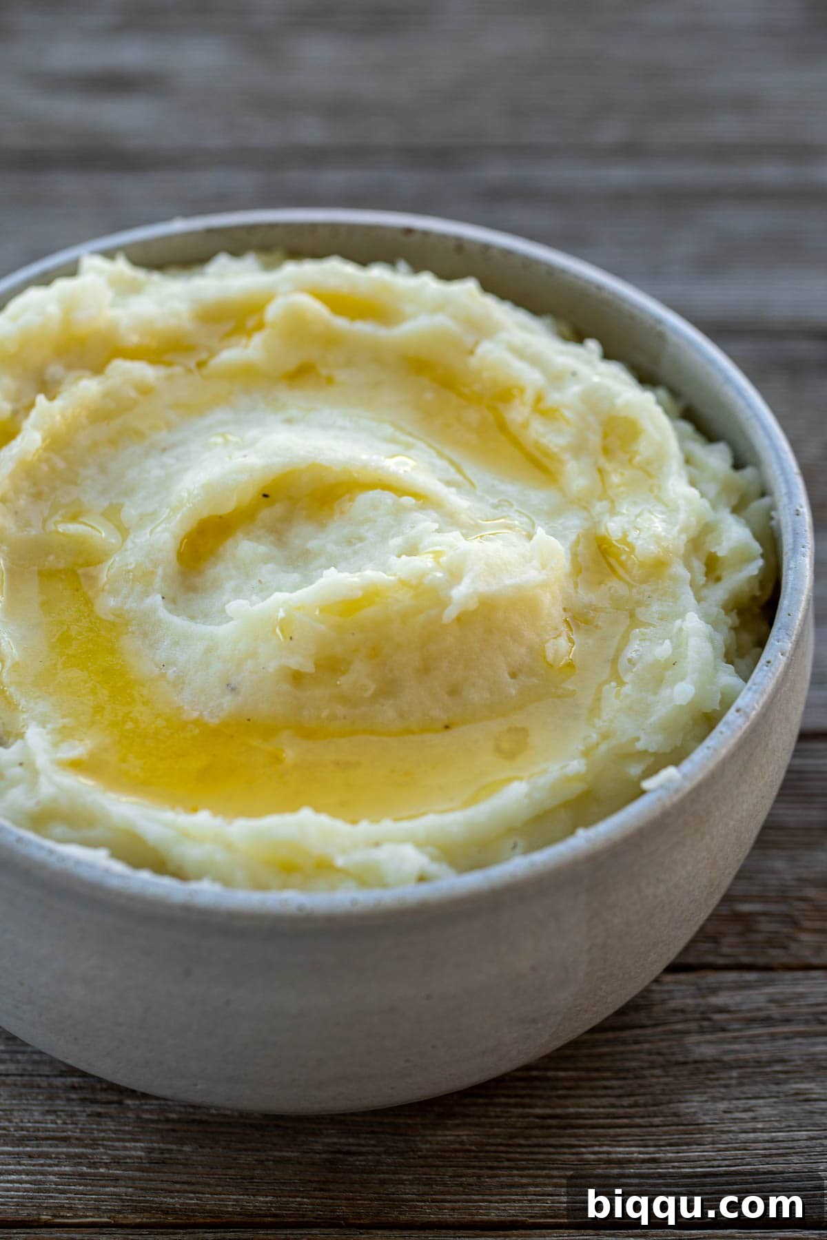 A rustic bowl of creamy buttermilk mashed potatoes, adorned with a pat of melted butter and a sprinkle of fresh herbs.