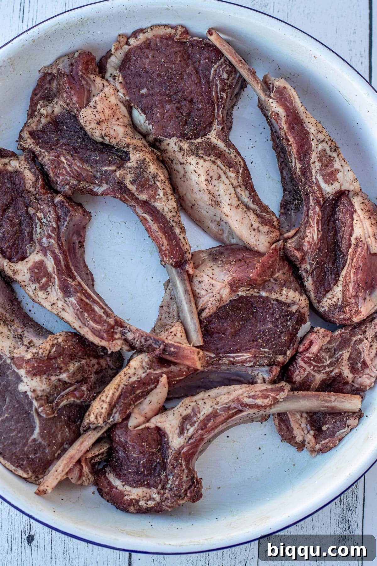 Seasoned lamb chops neatly arranged in a white bowl, ready for cooking.