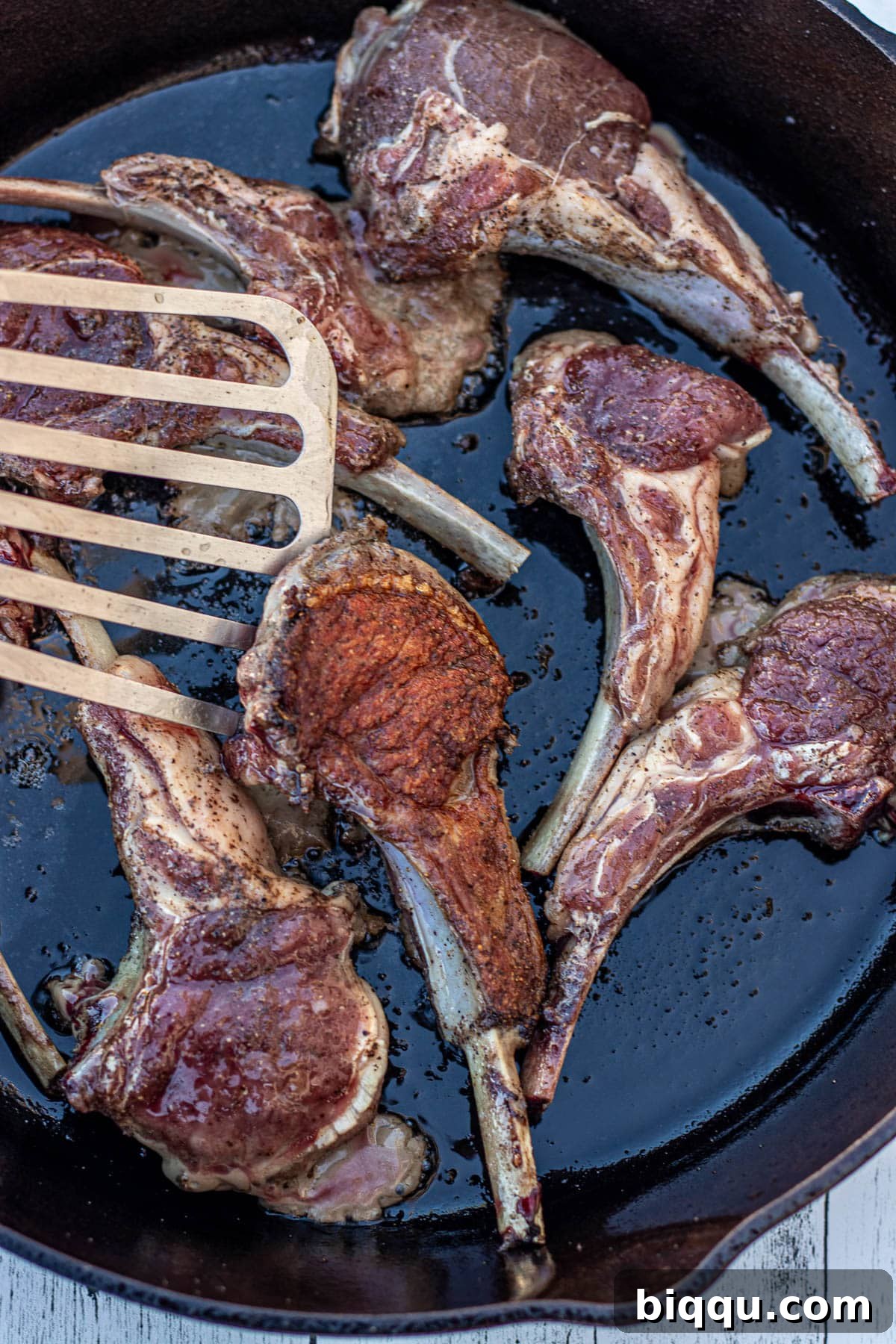 A fish spatula flipping a pan-seared lamb chop, showing a perfectly golden-brown crust.