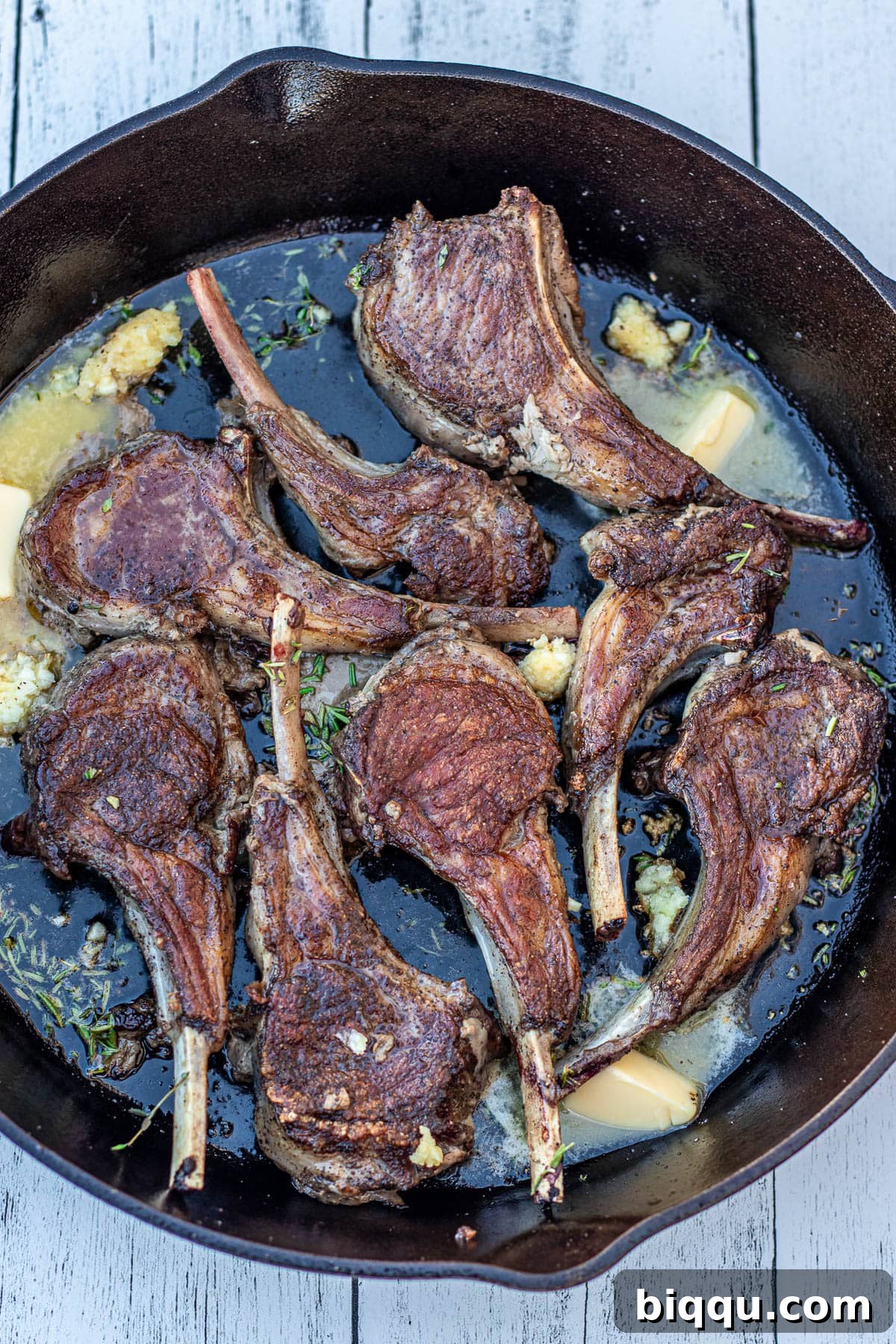 Flipped lamb chops with melting butter, minced garlic, and fresh herbs infusing the pan.