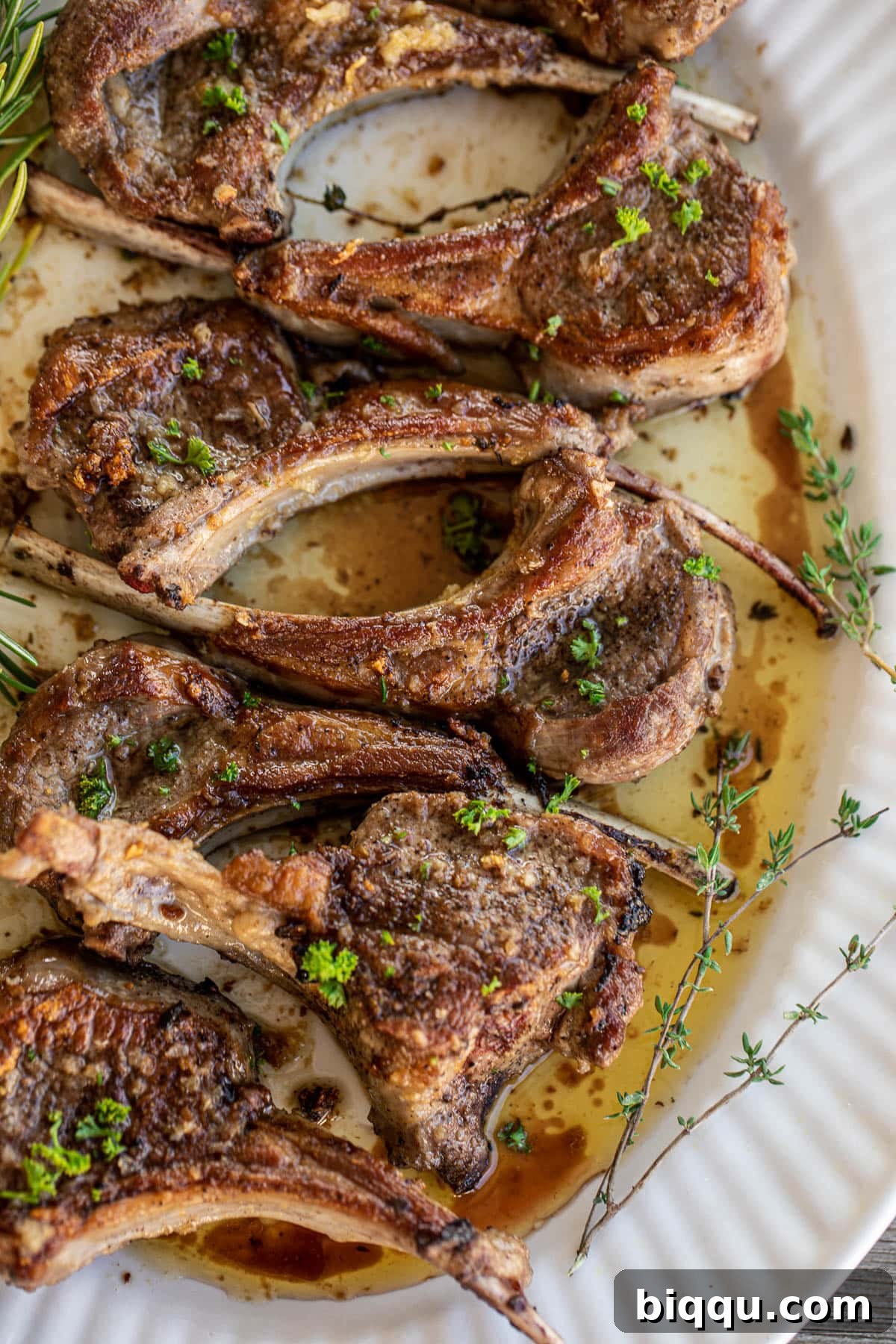 Pan seared lamb chops served on a large tray, beautifully garnished with fresh thyme and rosemary leaves.