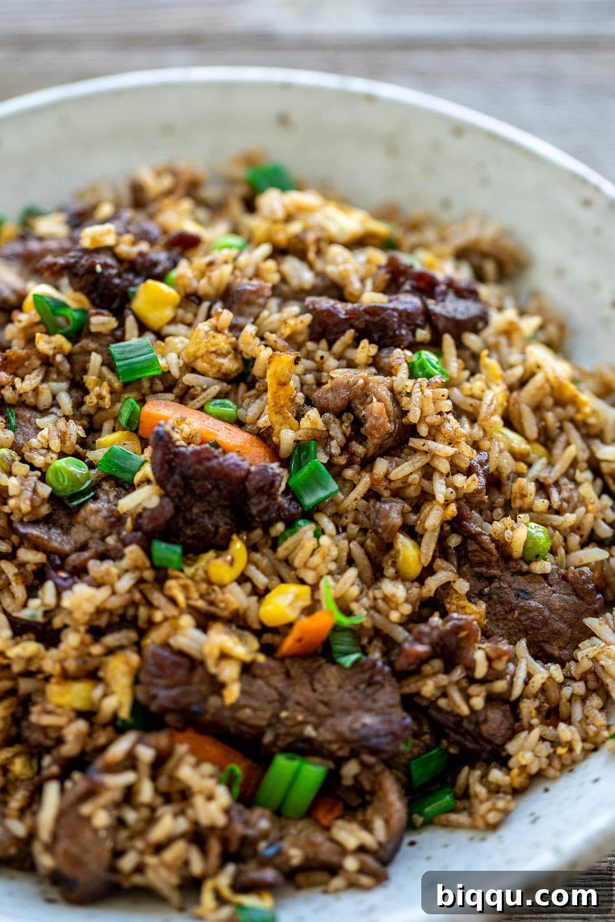 A serving of fried rice in a bowl, garnished with fresh green onions and other vibrant vegetables.