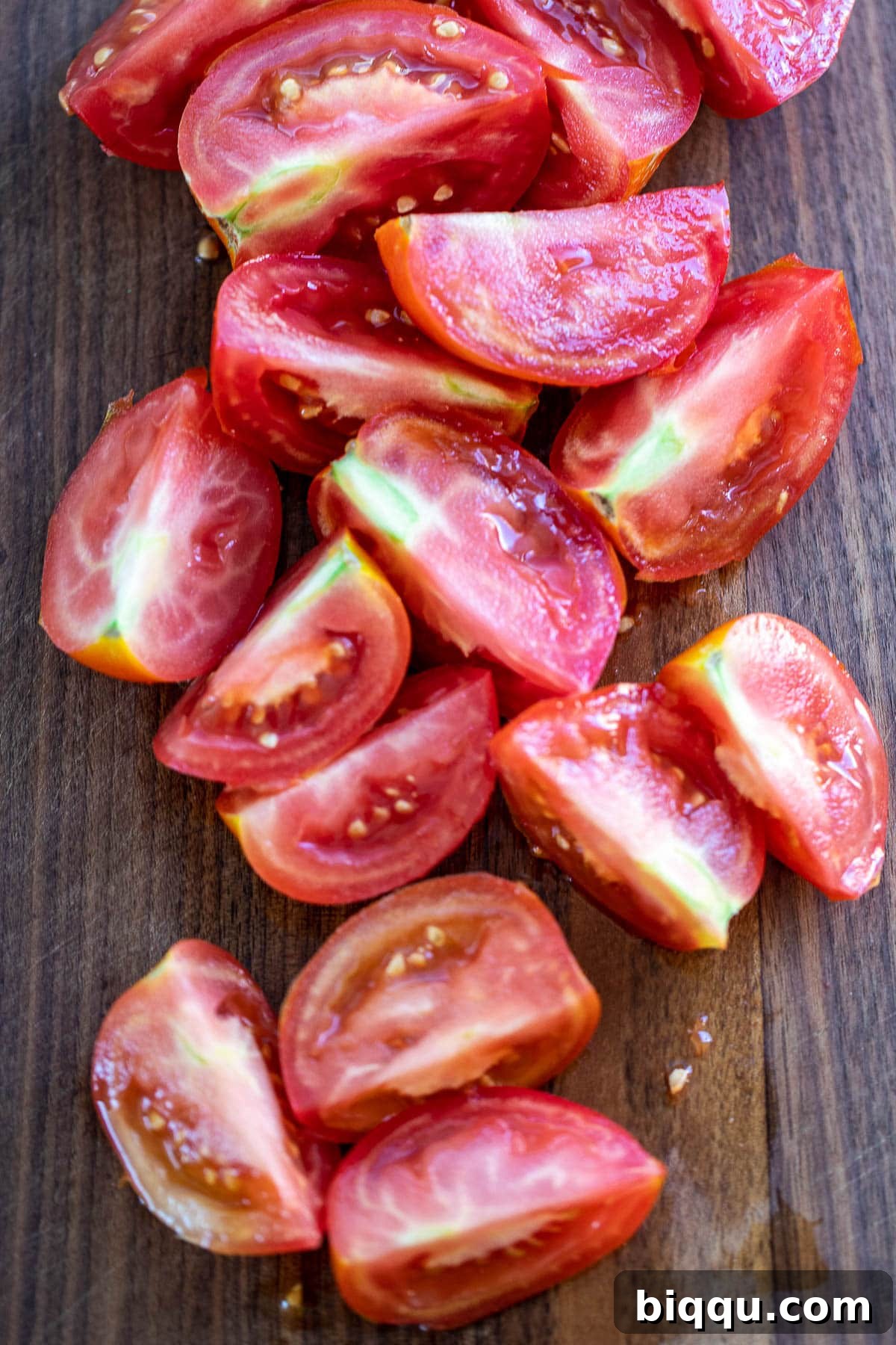 Quartered ripe tomatoes neatly arranged on a chopping board.