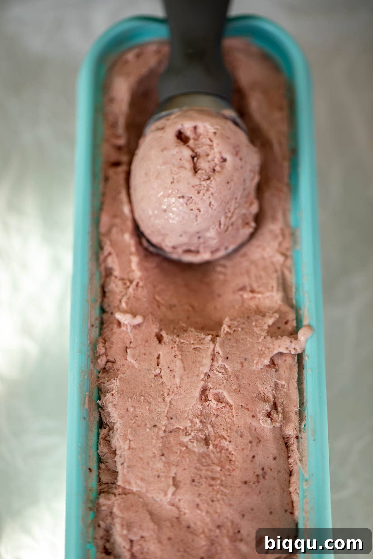 Creamy No-Churn Strawberry Dream 9 A perfectly formed scoop of homemade strawberry ice cream resting in a bowl of more ice cream, ready to serve.