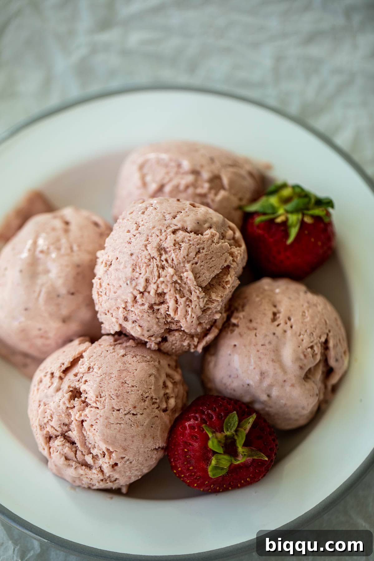 Creamy No-Churn Strawberry Dream 10 Scoops of creamy strawberry ice cream presented on a plate with fresh, ripe strawberries nearby, emphasizing its fresh ingredients.