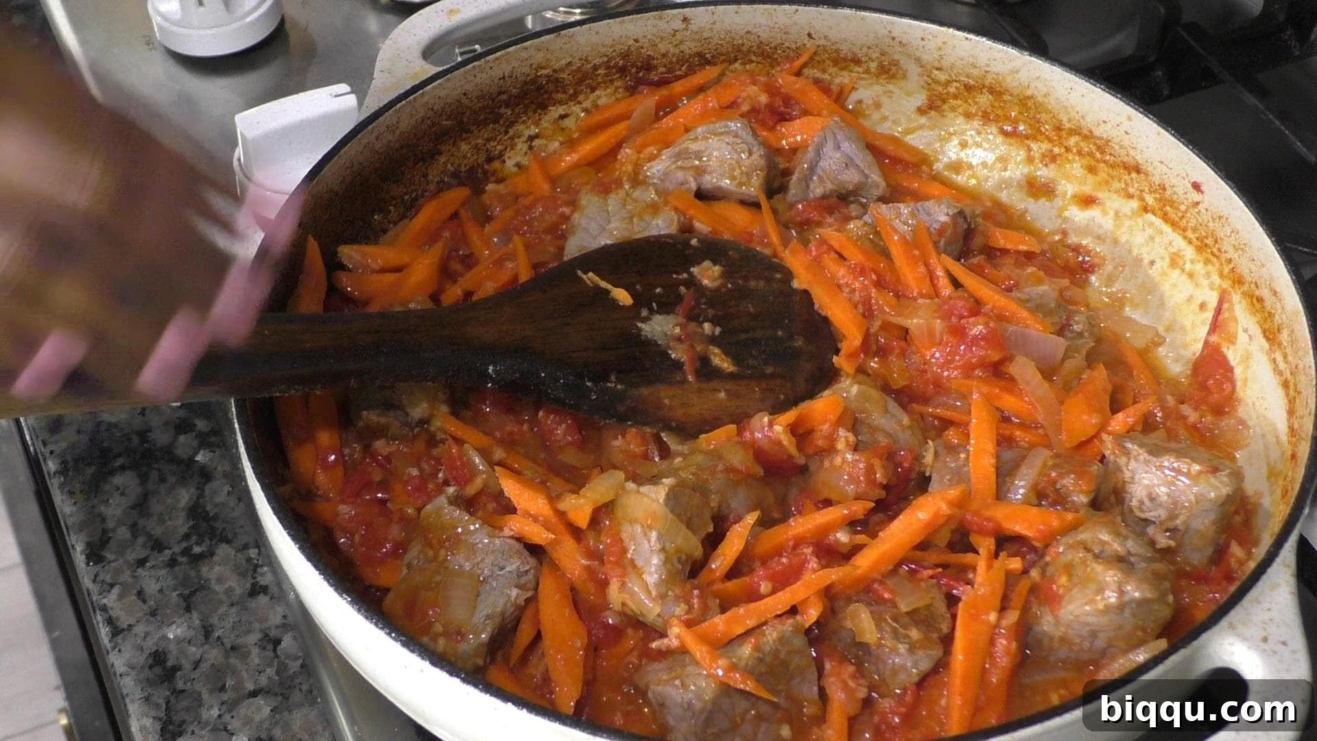 A pot filled with aromatic carrots and tender beef simmering in a rich tomato base, showcasing the stew's developing layers of flavor.