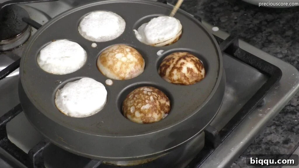 Cooking Vitumbua coconut rice pancakes on a special Aebleskiver pan over a stove.