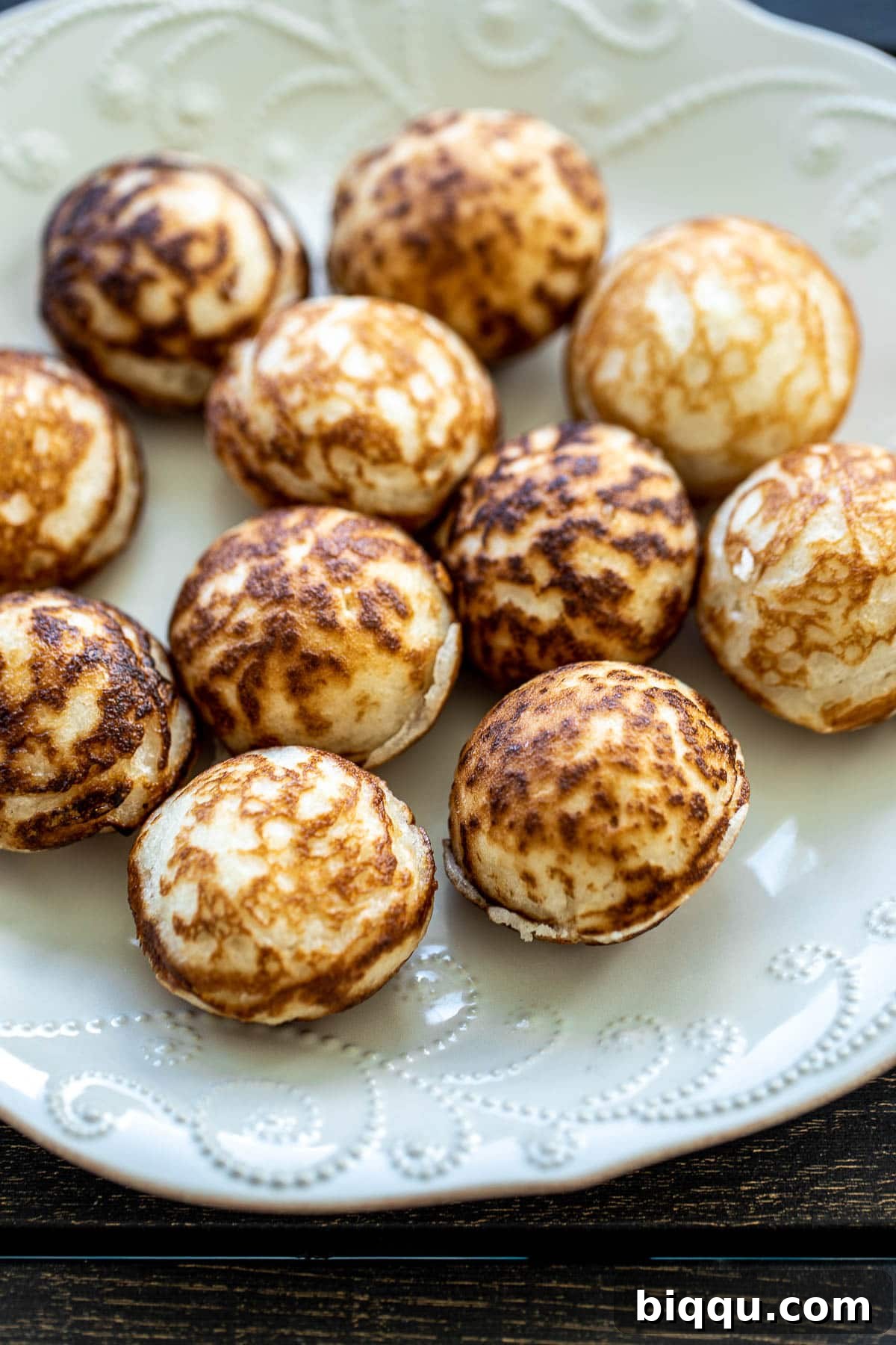 A stack of golden-brown Coconut Rice Pancakes (Vitumbua) on a white plate, ready to be enjoyed.
