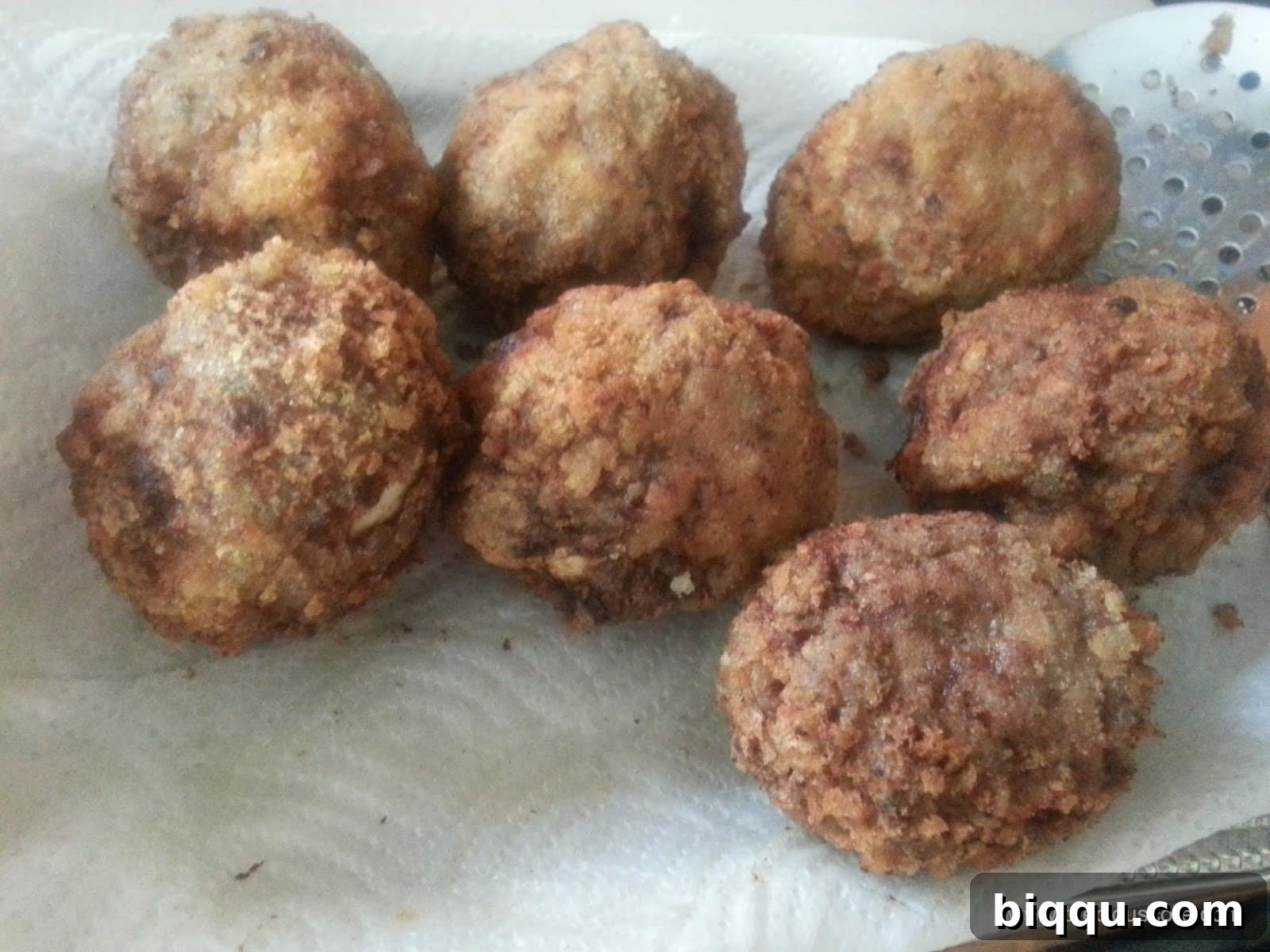 Freshly fried Scotch Eggs resting on paper towels to drain excess oil, highlighting their crispy texture.