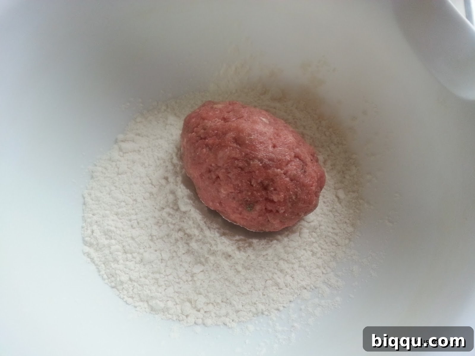 Hard-boiled egg expertly coated with seasoned ground meat, ready for the next dredging steps.