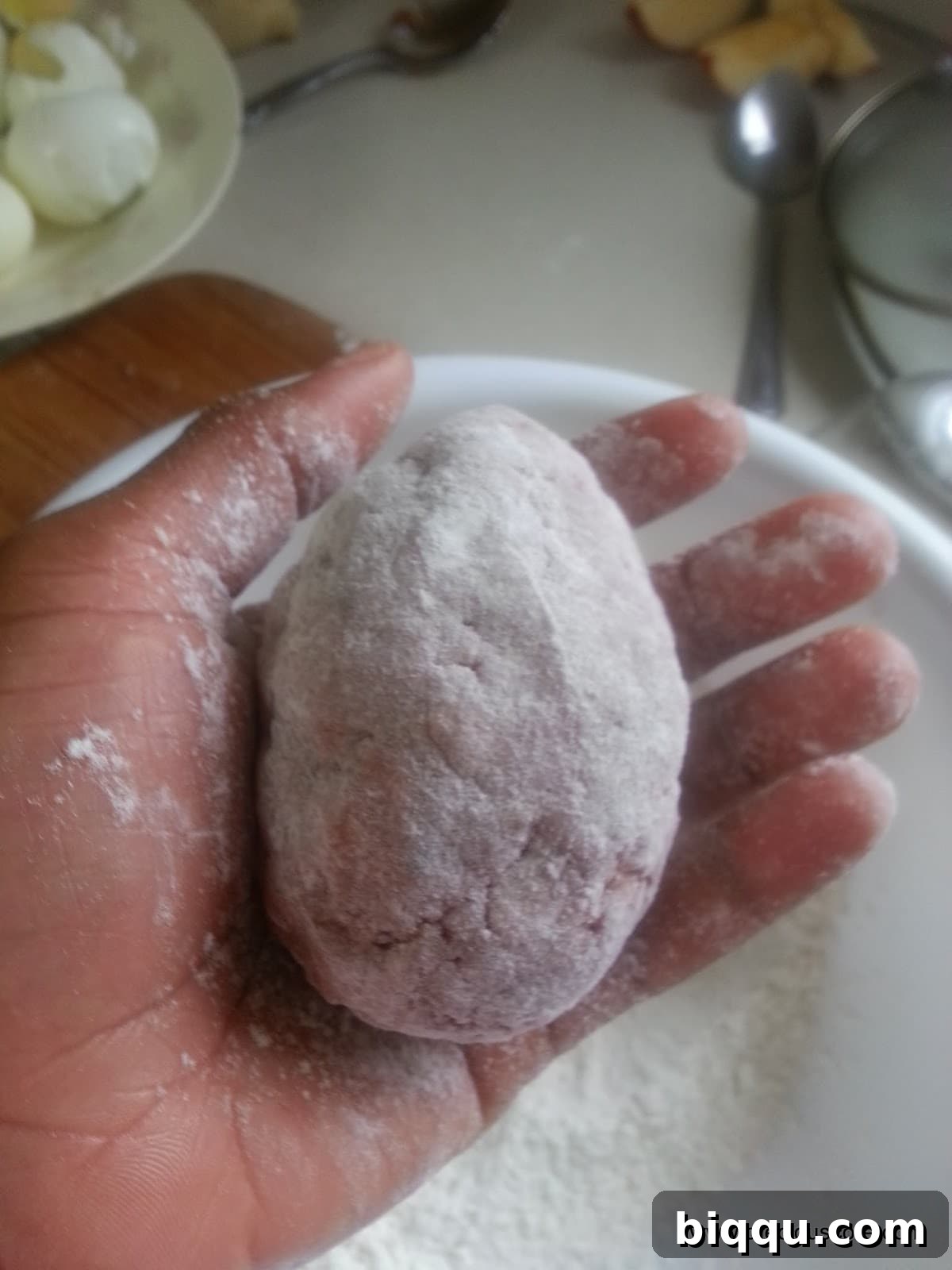 Meat-wrapped Scotch Egg being thoroughly dredged in all-purpose flour, ensuring an even coating.