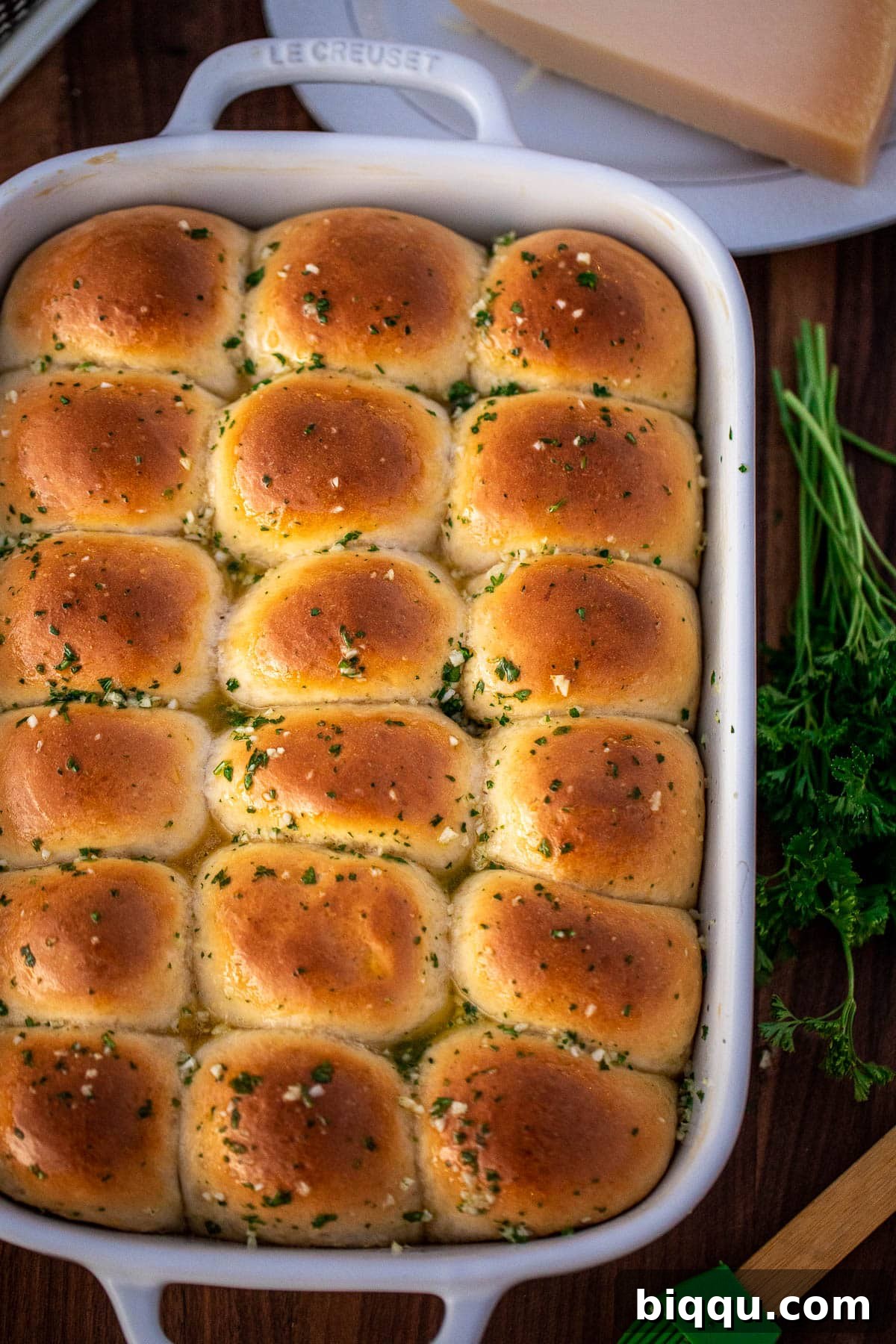 A full baking dish of golden-brown dinner rolls brushed generously with melted garlic butter, fresh parsley visible on top.