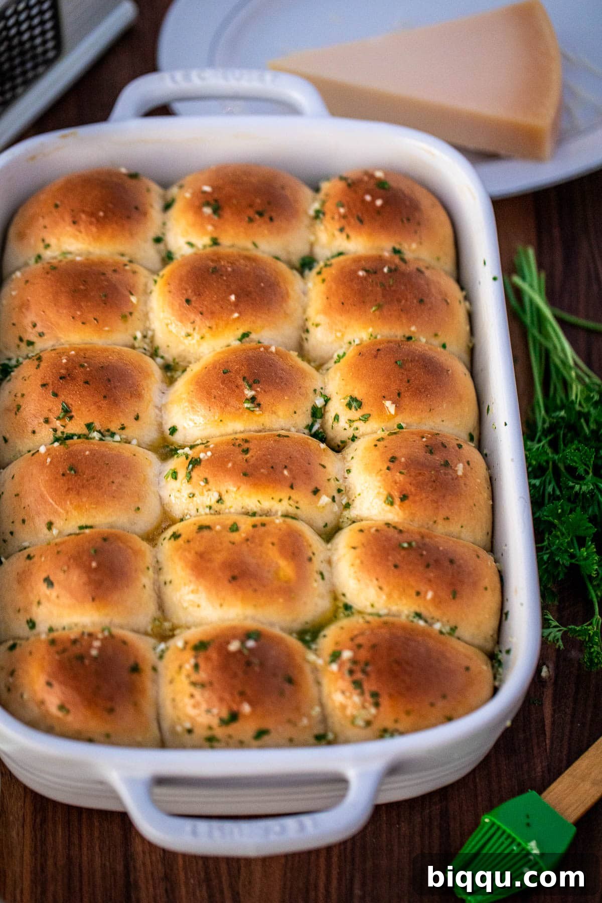 A complete baking dish of garlic dinner rolls, glistening with butter and sprinkled with parsley, ready to be served.