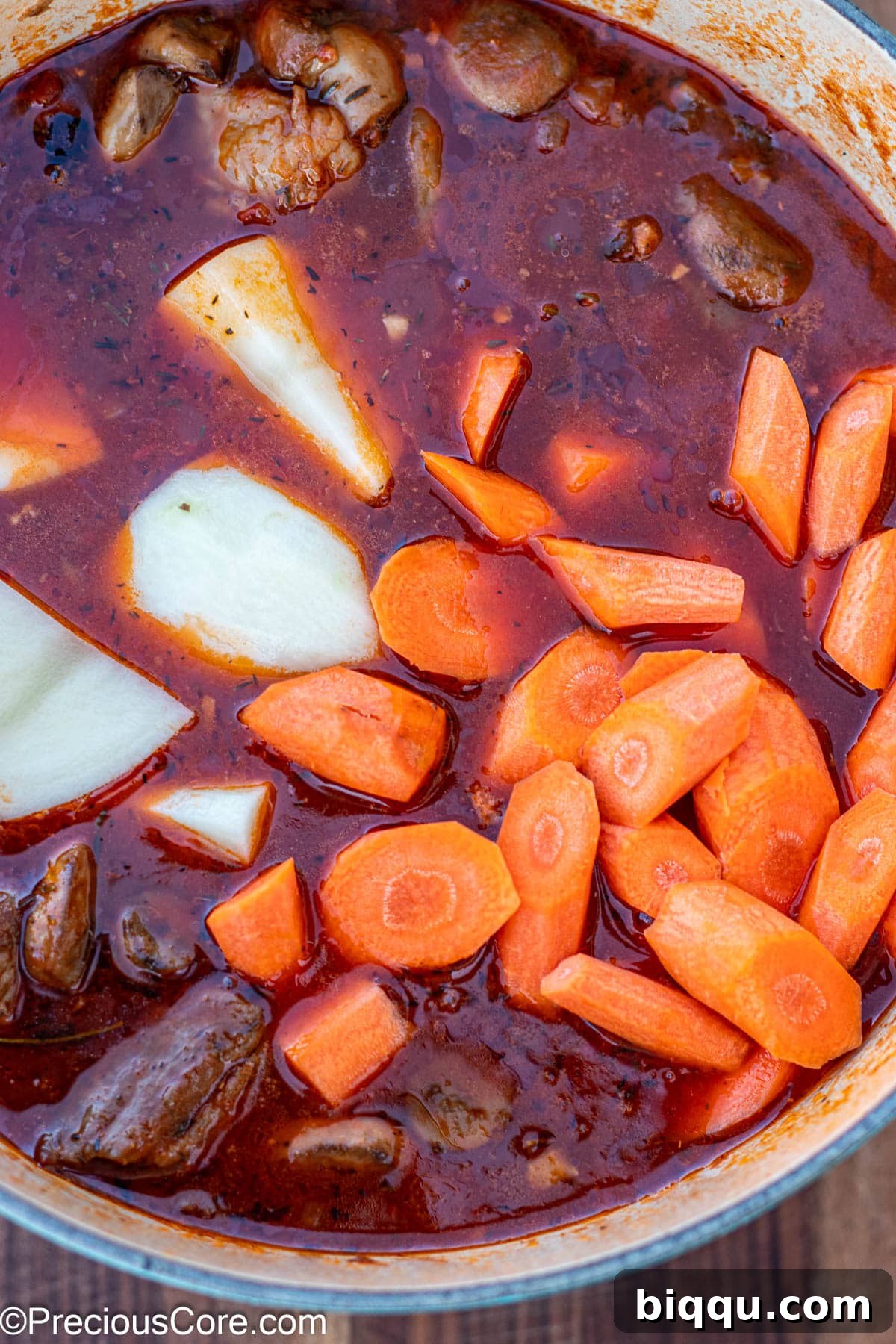 Hearty Beef Stew 11 Raw carrots and potatoes added to a pot of stew, awaiting further cooking.