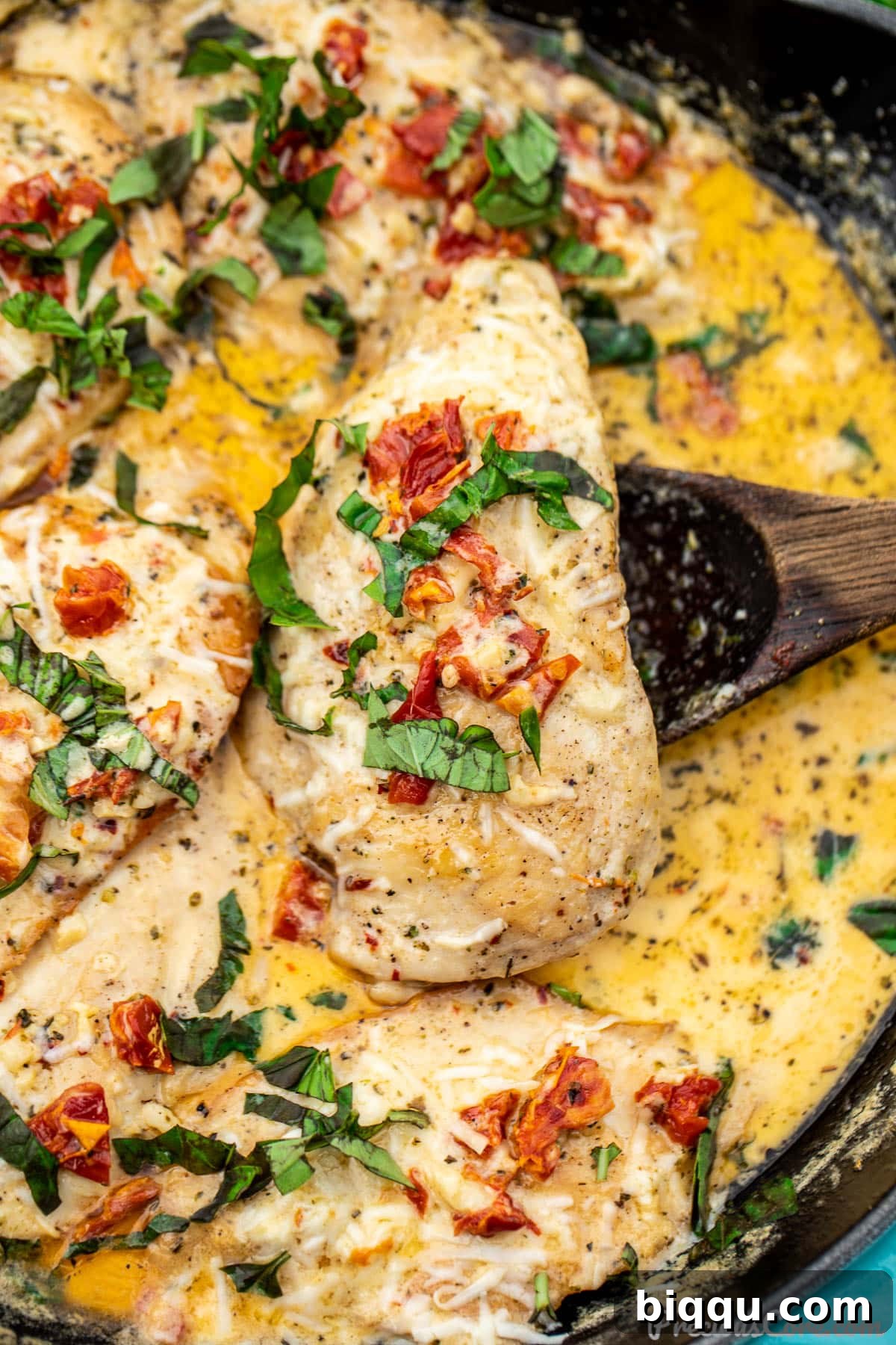 A perfectly cooked piece of Marry Me Chicken breast nestled in its rich, creamy sun-dried tomato sauce, ready to be served. A wooden spoon gently holds the chicken.
