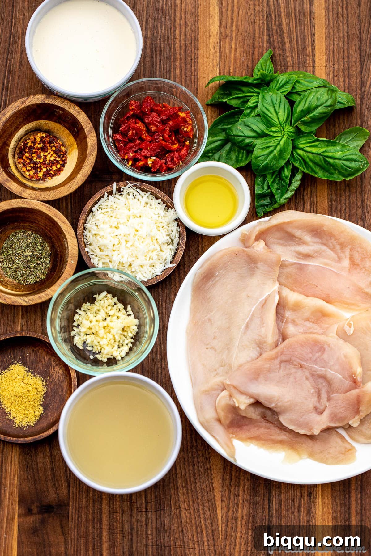 Fresh ingredients for Marry Me Chicken laid out on a rustic chopping board, including chicken breasts, sun-dried tomatoes, fresh basil, garlic, and heavy cream.