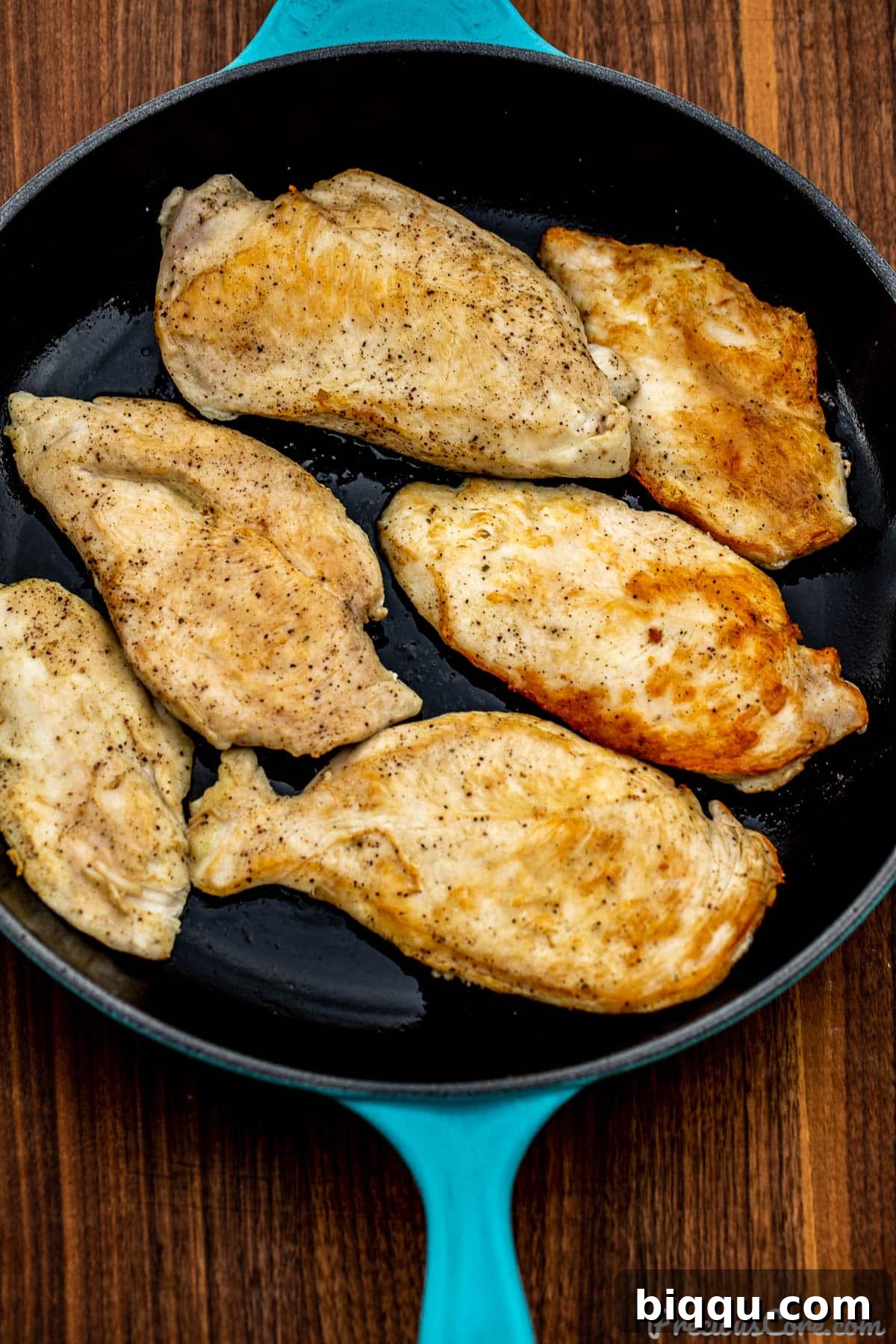 Golden-brown pan-seared chicken breasts cooking in a large skillet.