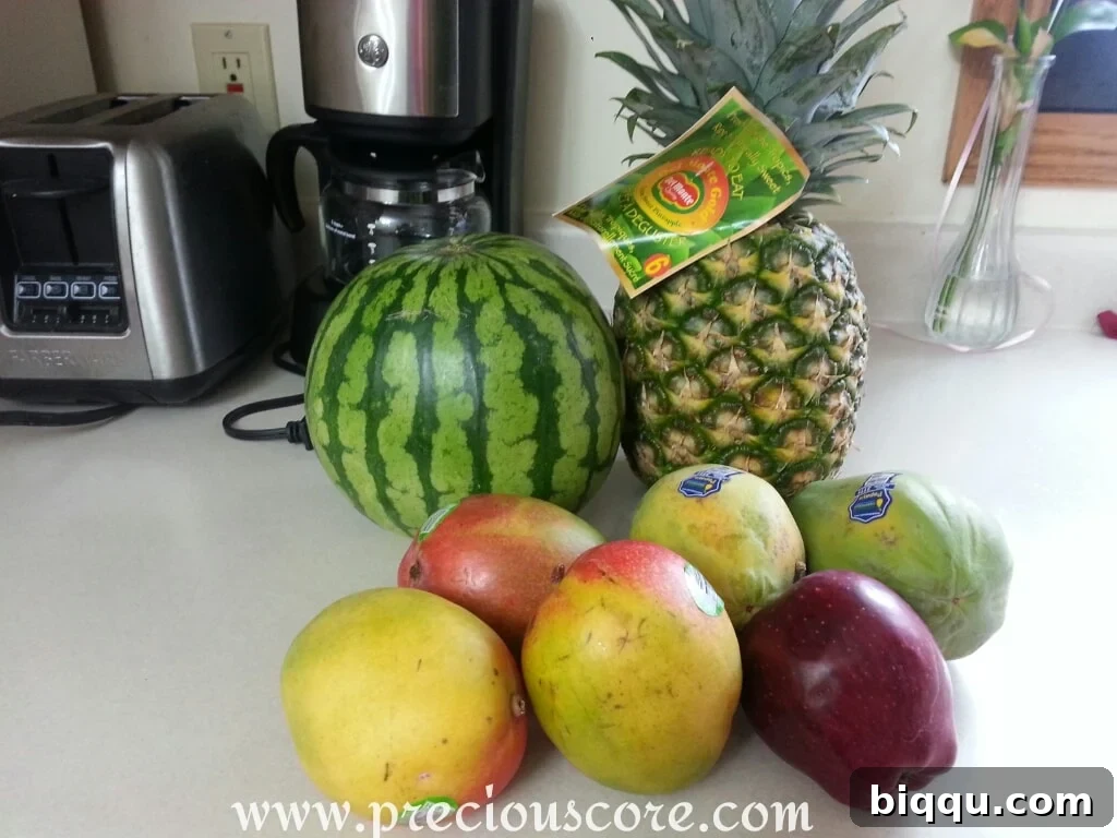 Ingredients for a tropical fruit salad, featuring pineapple, papaya, mangoes, watermelon, and apple