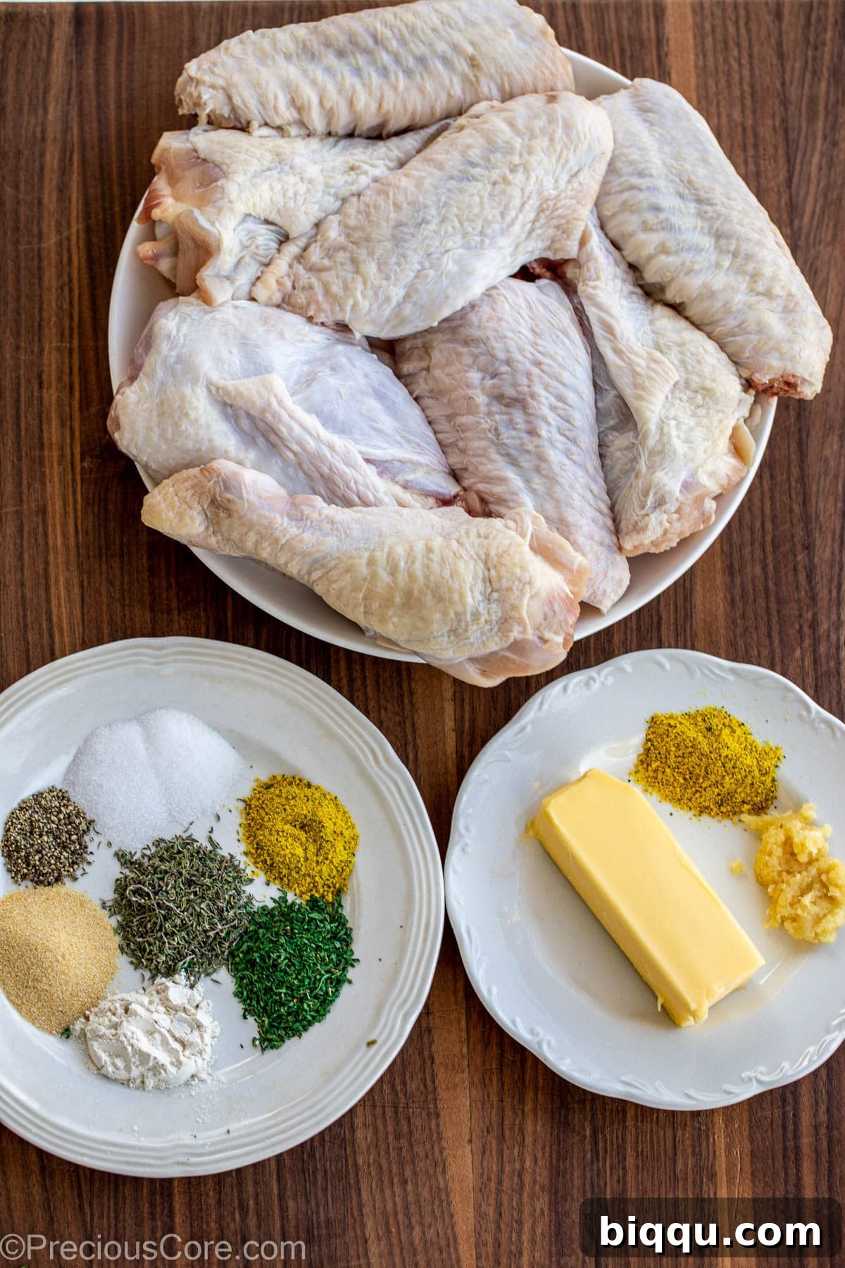 Raw turkey wings, an assortment of spices, and a stick of butter neatly arranged on a wooden chopping board.