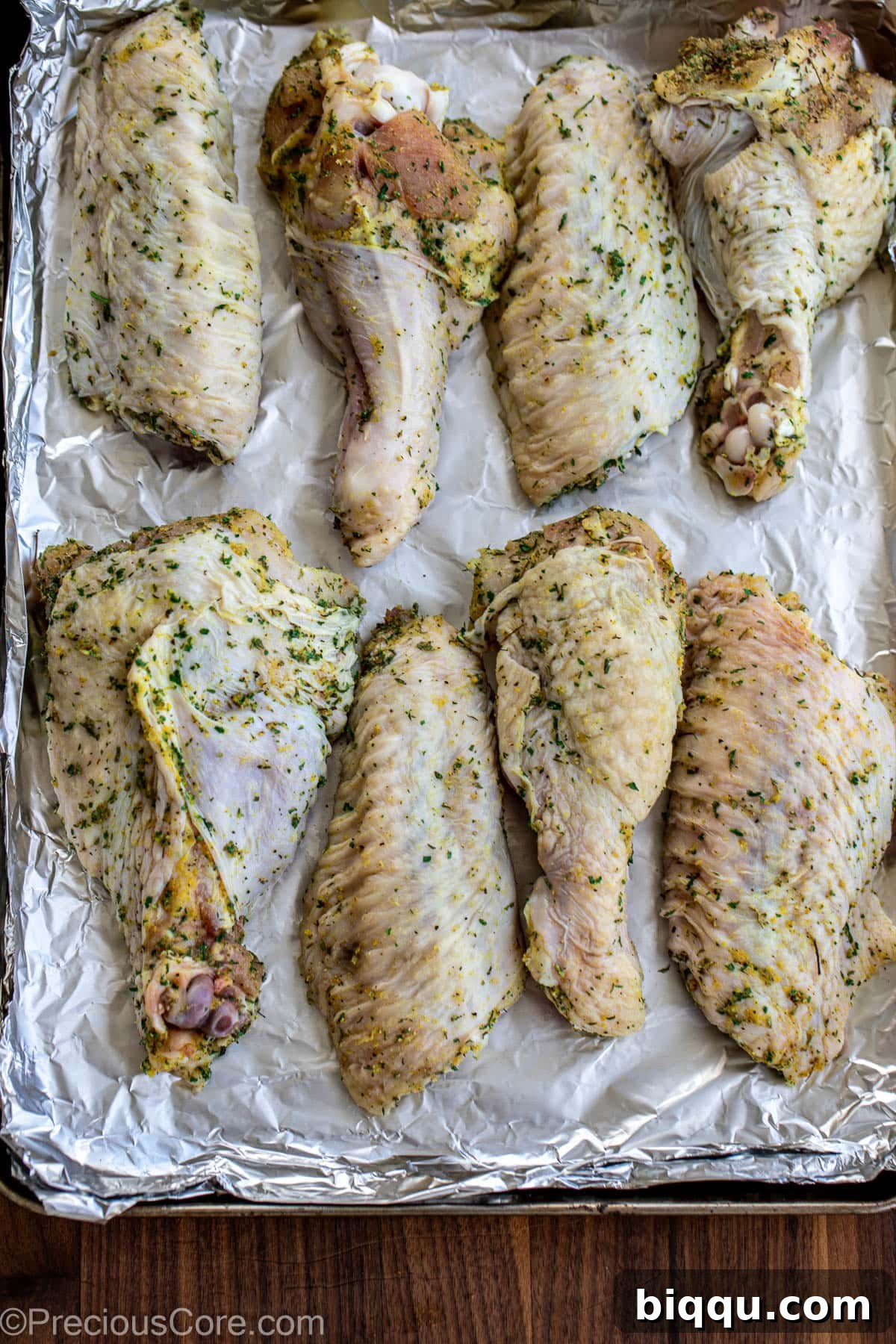 Raw turkey wings generously seasoned with a dry rub on a baking sheet, ready for the oven.