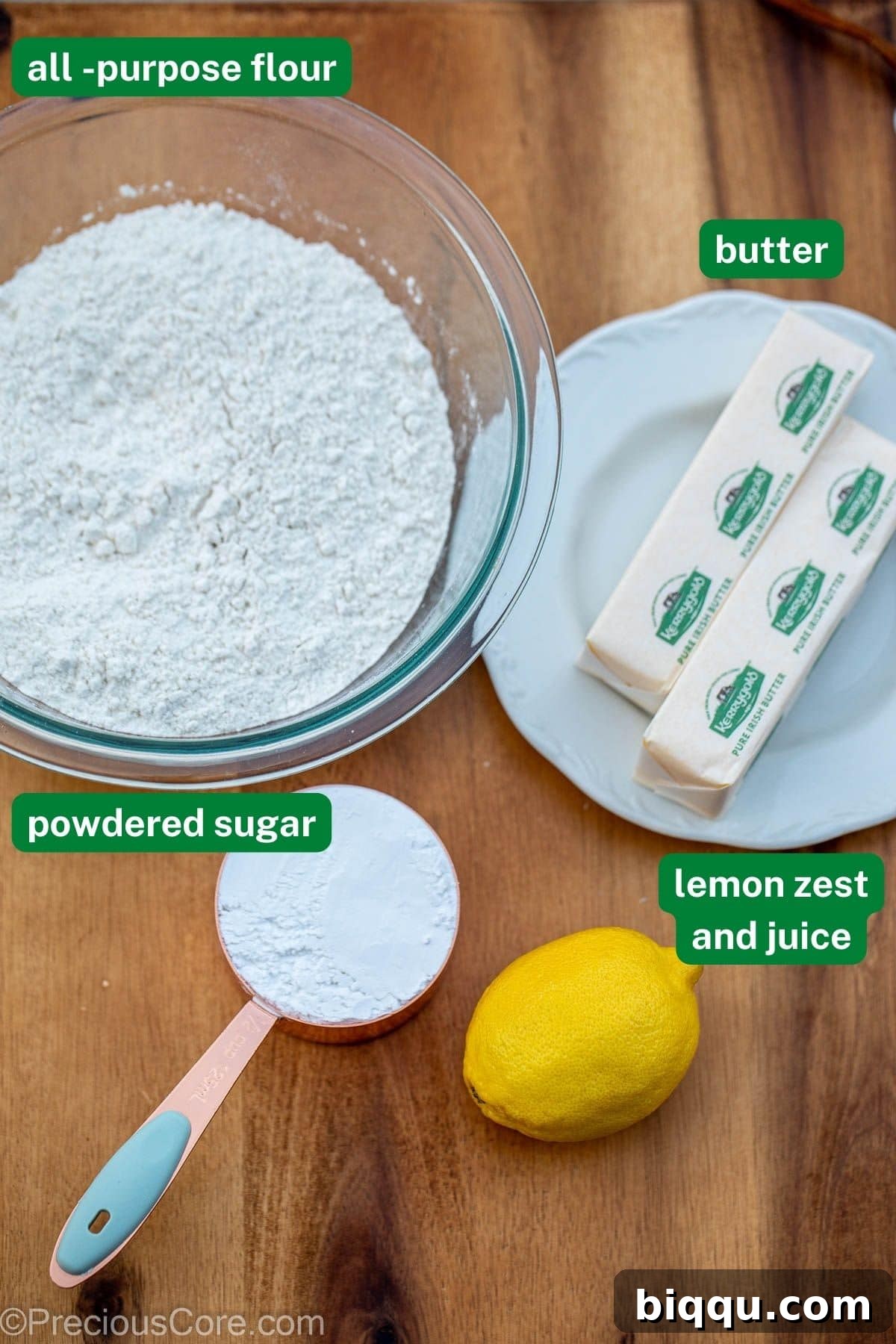 Flour, butter, powdered sugar, and fresh lemons neatly arranged on a wooden chopping board.