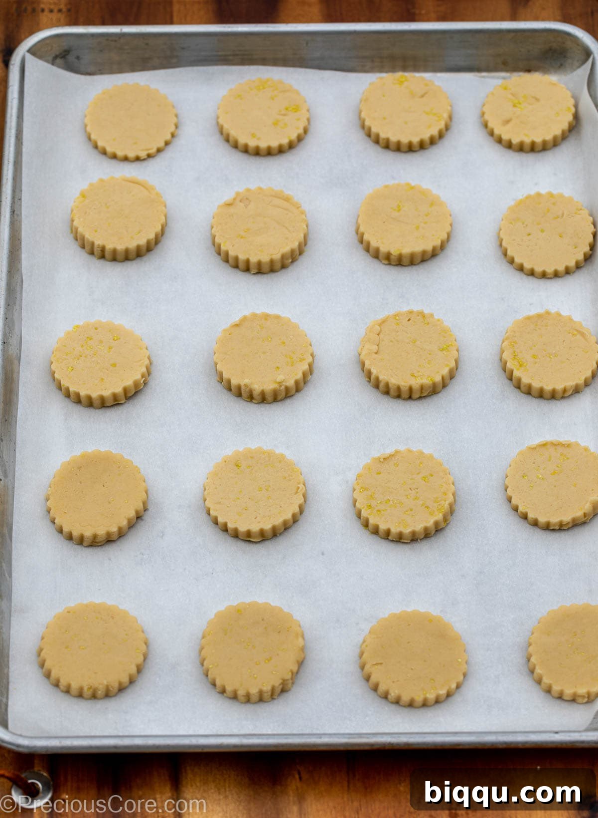 Neatly cut-out lemon shortbread cookie dough pieces placed on a baking sheet lined with parchment paper.