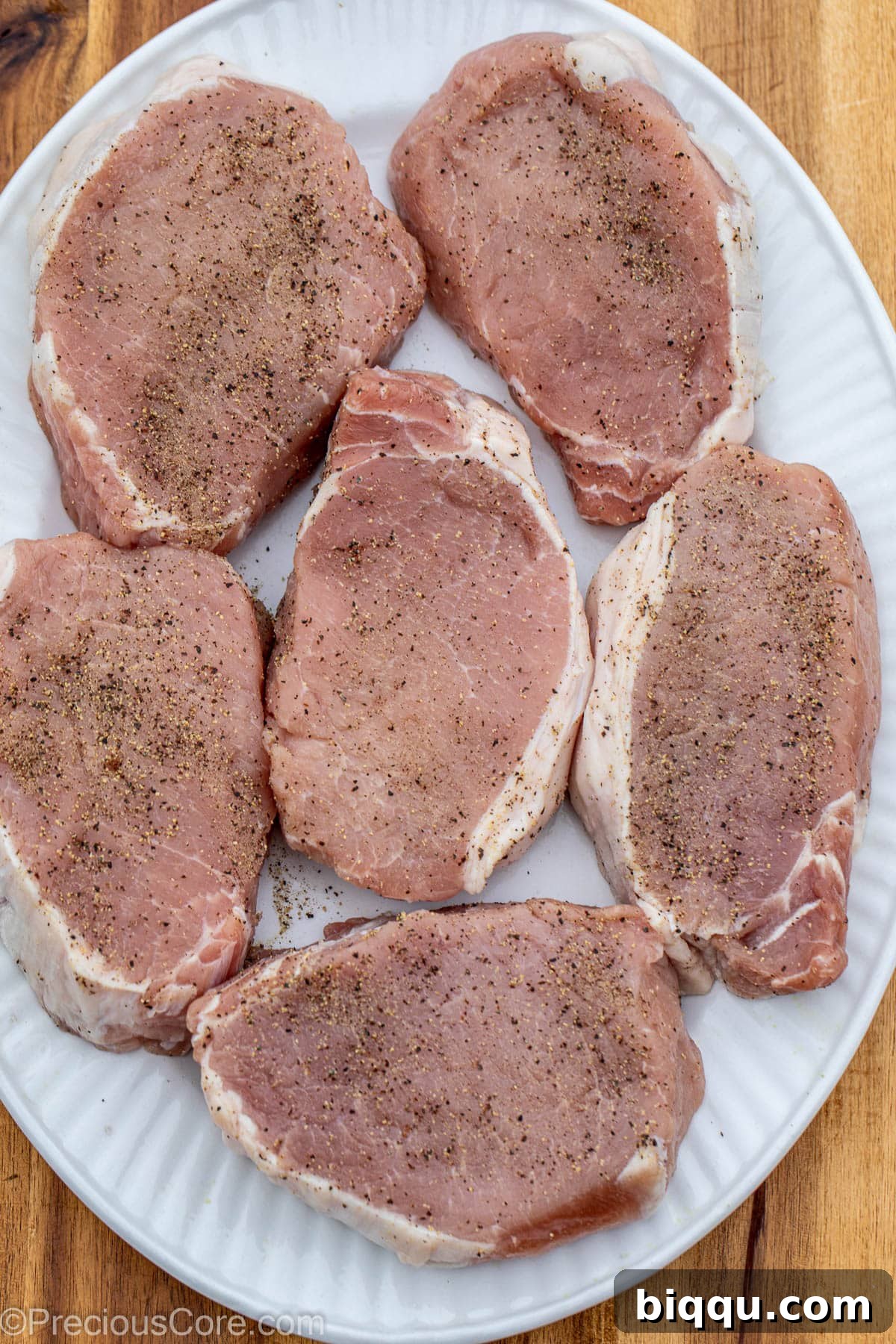Pork chops in pan, seasoned with salt and pepper.