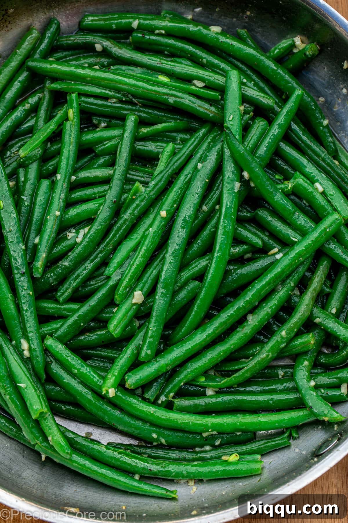 A cast iron skillet filled with perfectly cooked, vibrant green beans generously coated in glistening garlic butter and ready to be served.