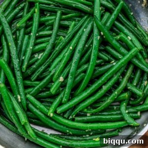 Square image of vibrant garlic butter green beans in a bowl, showcasing their appealing color and texture.
