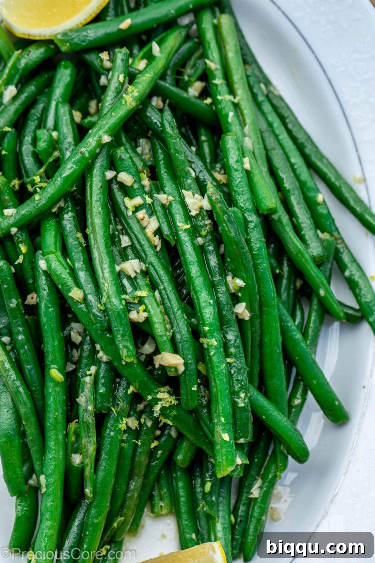 A close-up shot of vibrant green beans coated in garlic butter and garnished with fresh herbs, served on an elegant white serving tray.