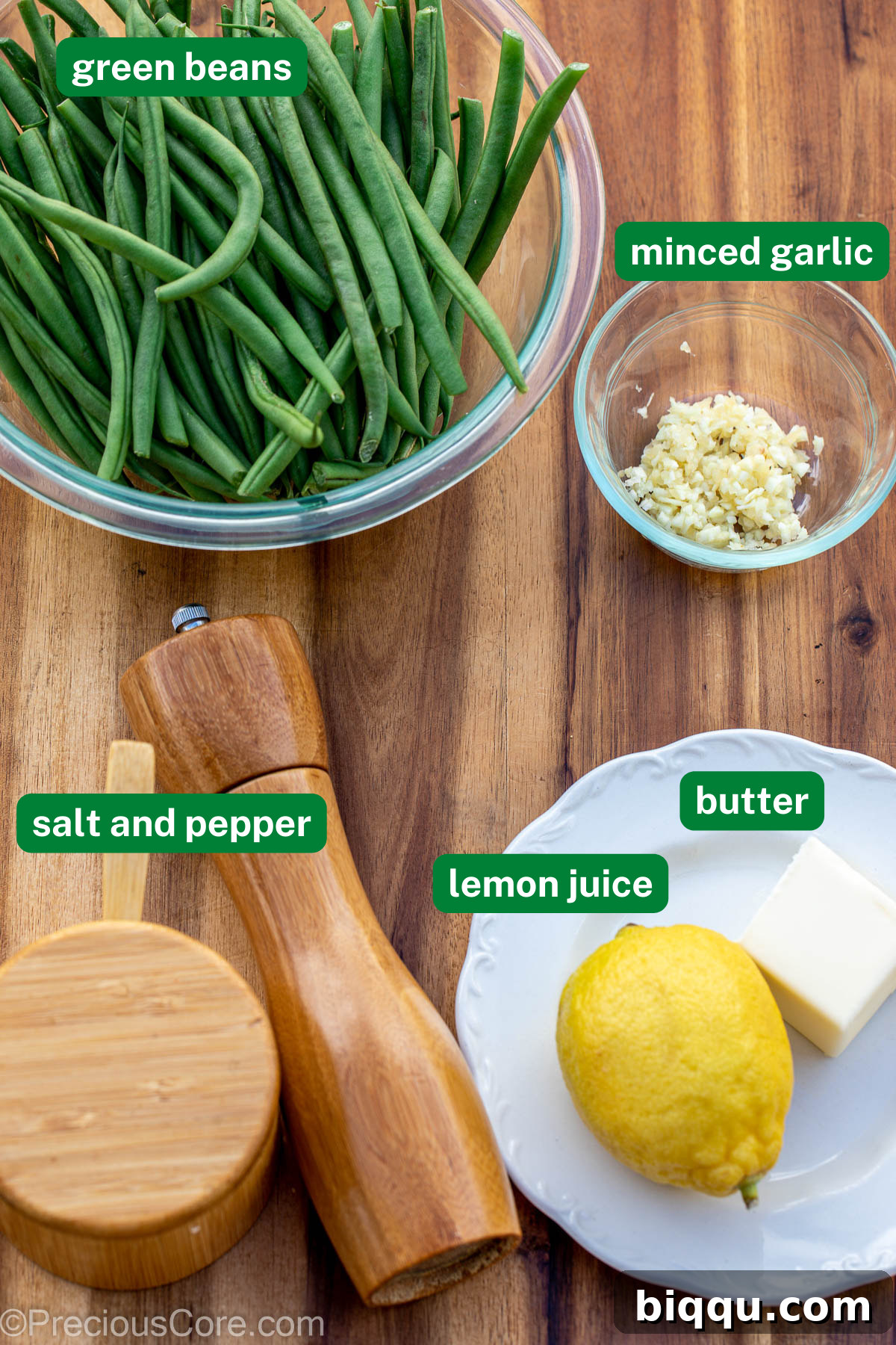 Fresh green beans, finely minced garlic, a pinch of salt and black pepper, a whole lemon, and a stick of unsalted butter neatly arranged on a rustic wooden chopping board.