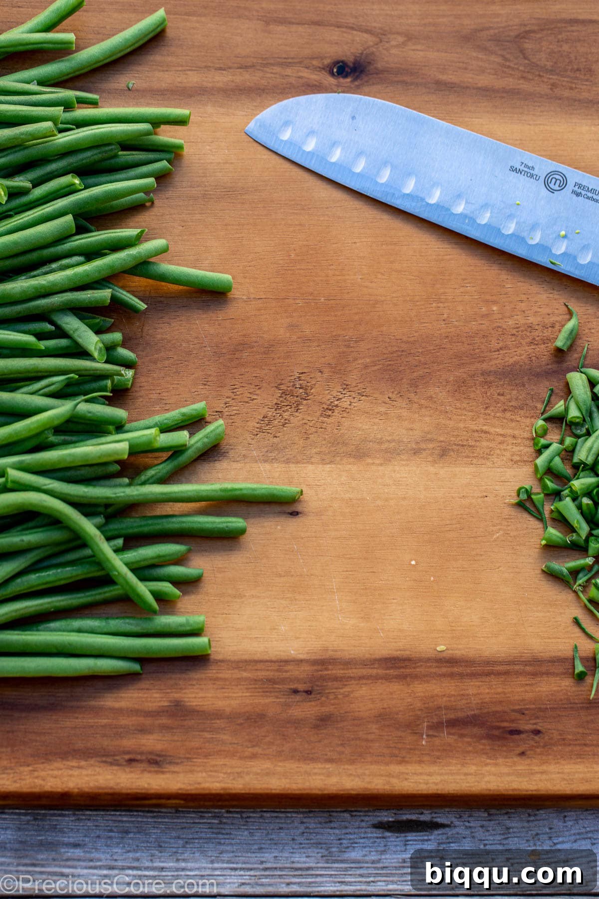 Fresh, untrimmed green beans neatly arranged on a wooden chopping board, ready for preparation.
