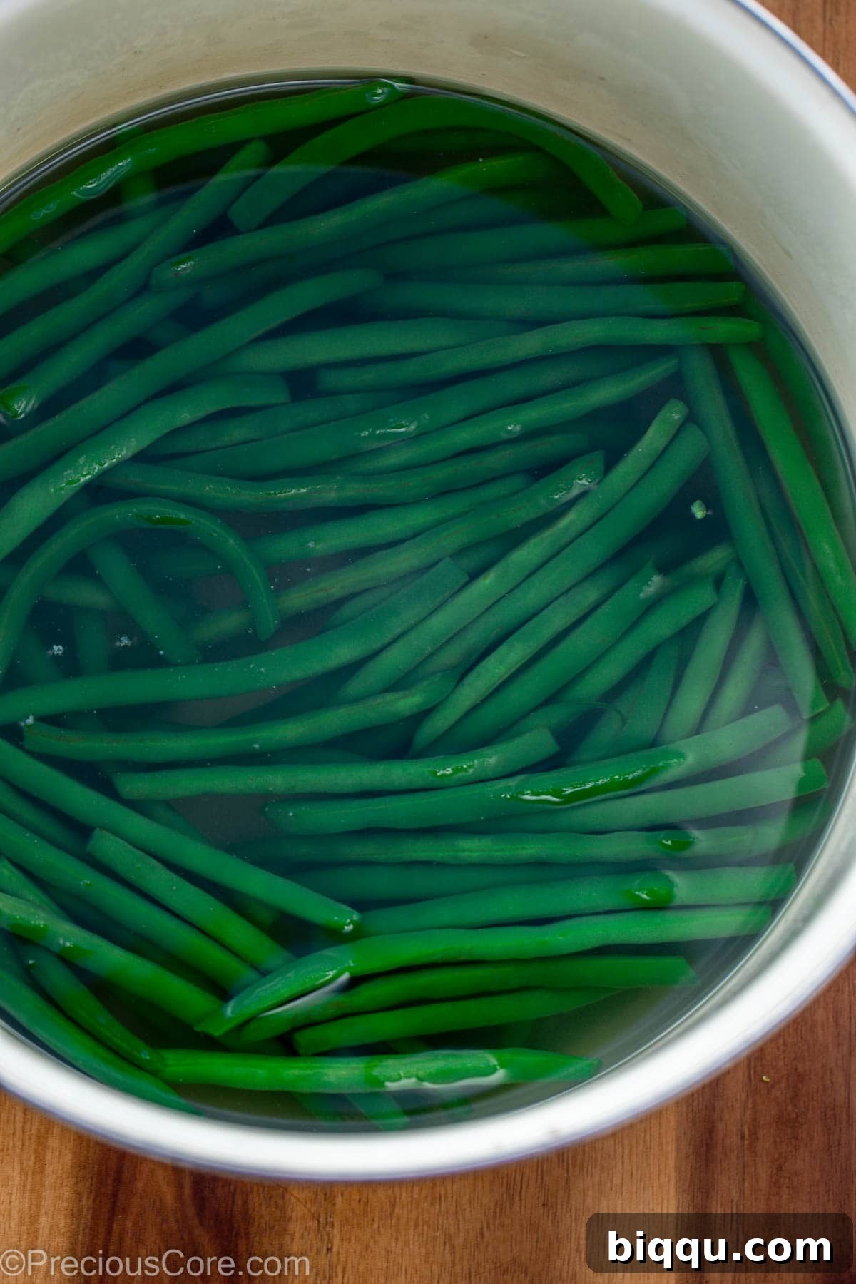 Fresh green beans immersed in a pot of vigorously boiling water, indicating the blanching process.