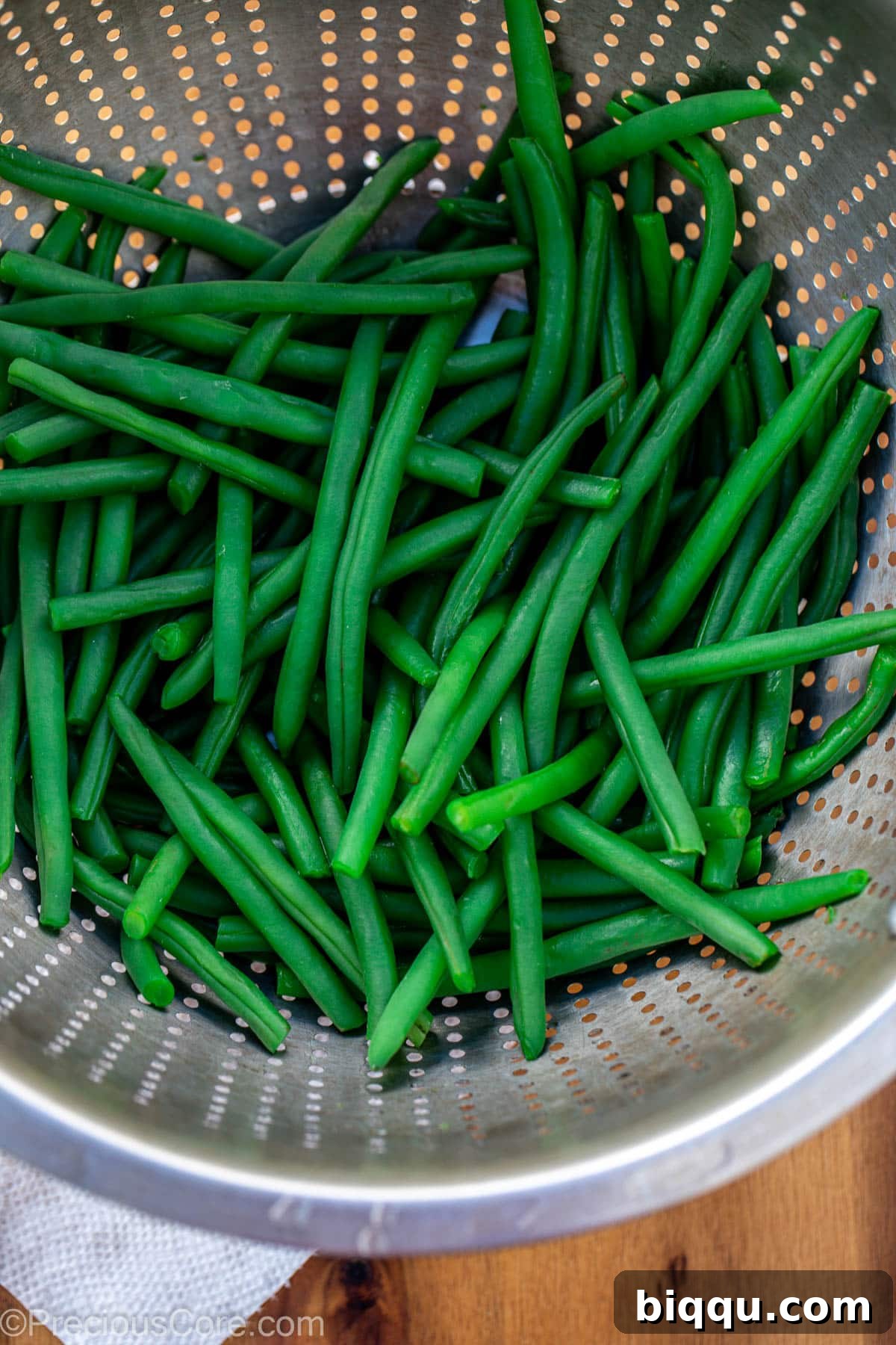 Steaming, blanched green beans being drained in a white colander, removing excess water.