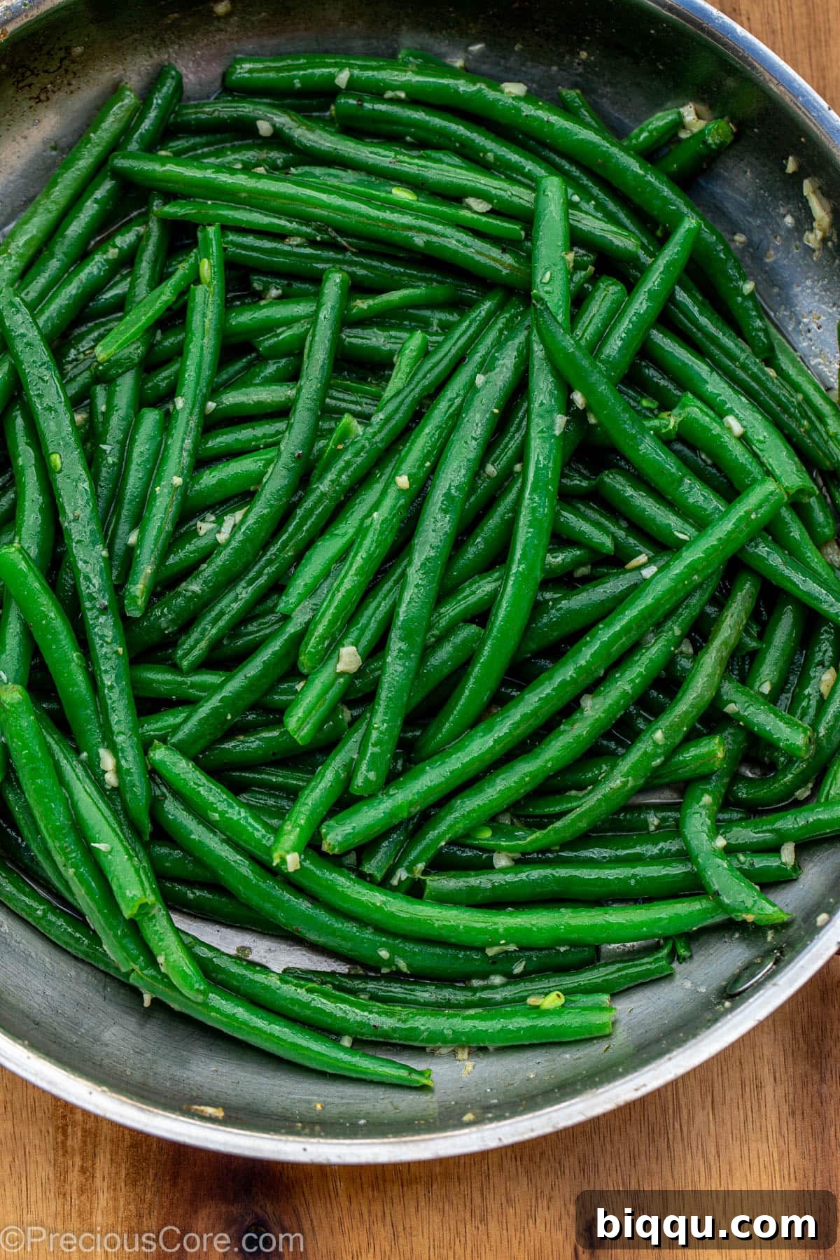 Blanched green beans being tossed vigorously with fragrant garlic butter in a large skillet, ensuring even coating.