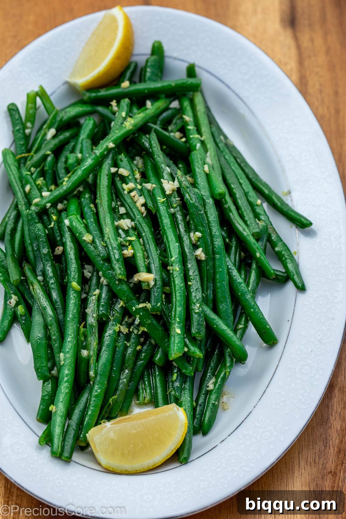 Beautifully prepared garlic butter green beans on a pristine white serving tray, elegantly garnished with fresh lemon slices and zest, ready for the table.