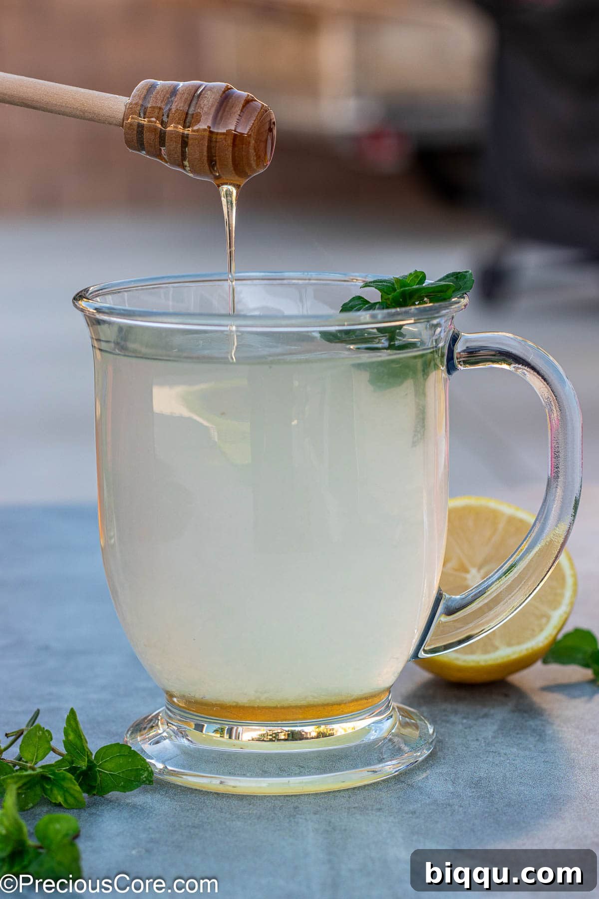 A honey dipper slowly dripping golden honey into a steaming mug of freshly made honey lemon tea, creating a comforting swirl.