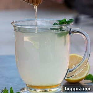 A honey dipper dripping honey into a cup of honey lemon tea, ready to be stirred and enjoyed.