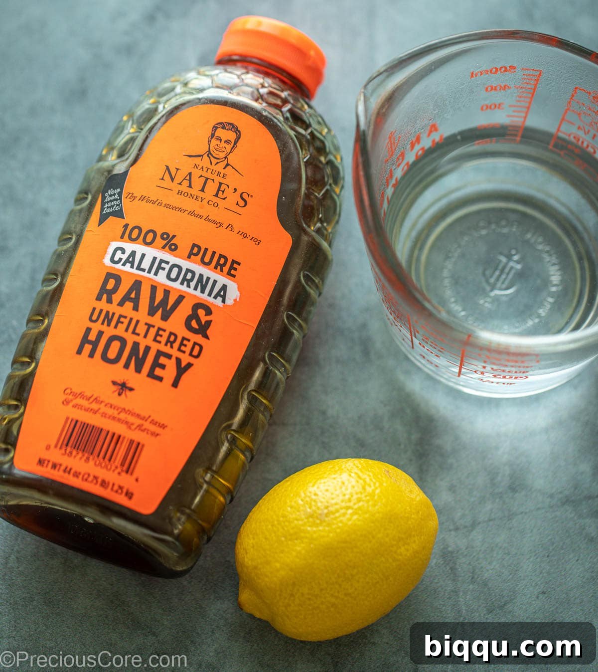 A visual display of the key ingredients for honey lemon tea: a jar of golden honey, a vibrant yellow lemon, and a mug filled with clear water.