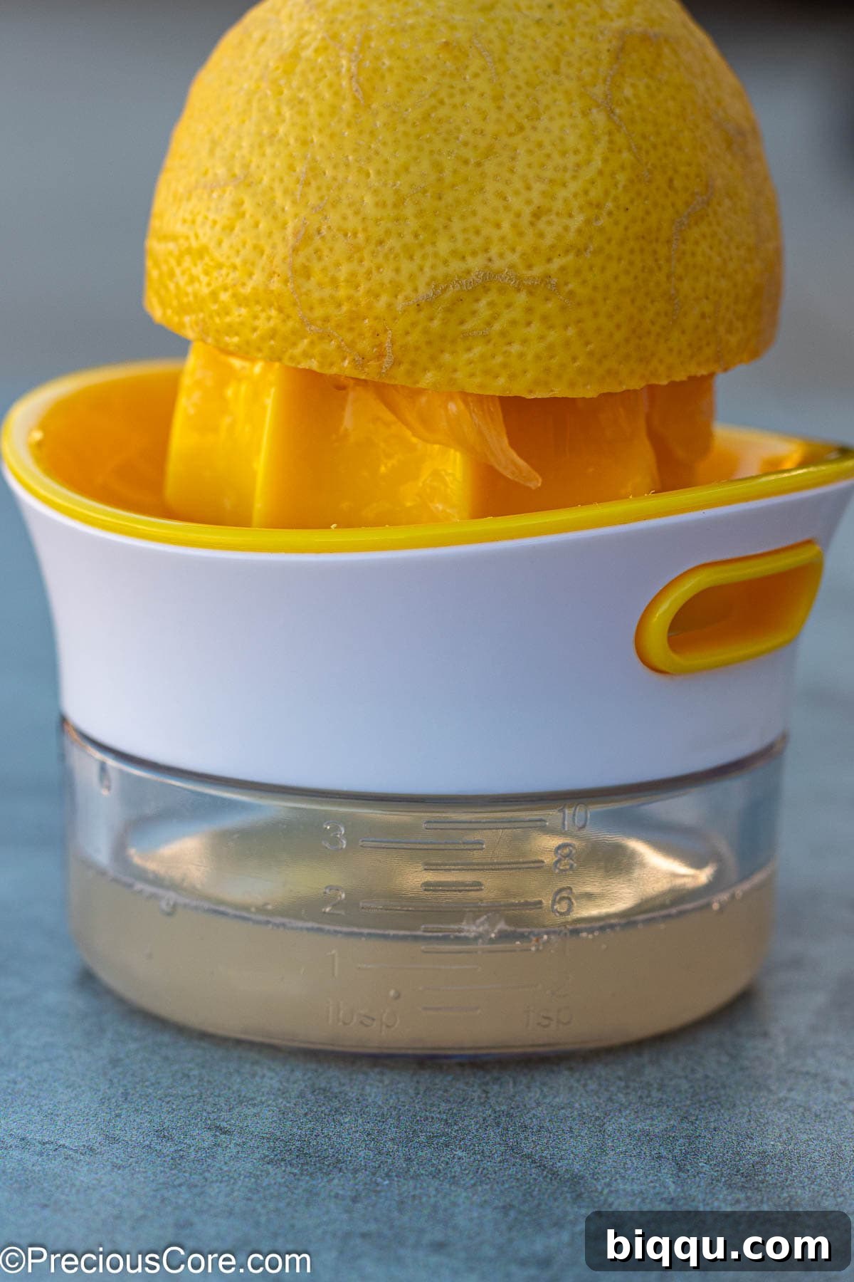 Fresh lemon juice being squeezed into a measuring cup using a manual lemon squeezer, showing the vibrant yellow liquid.