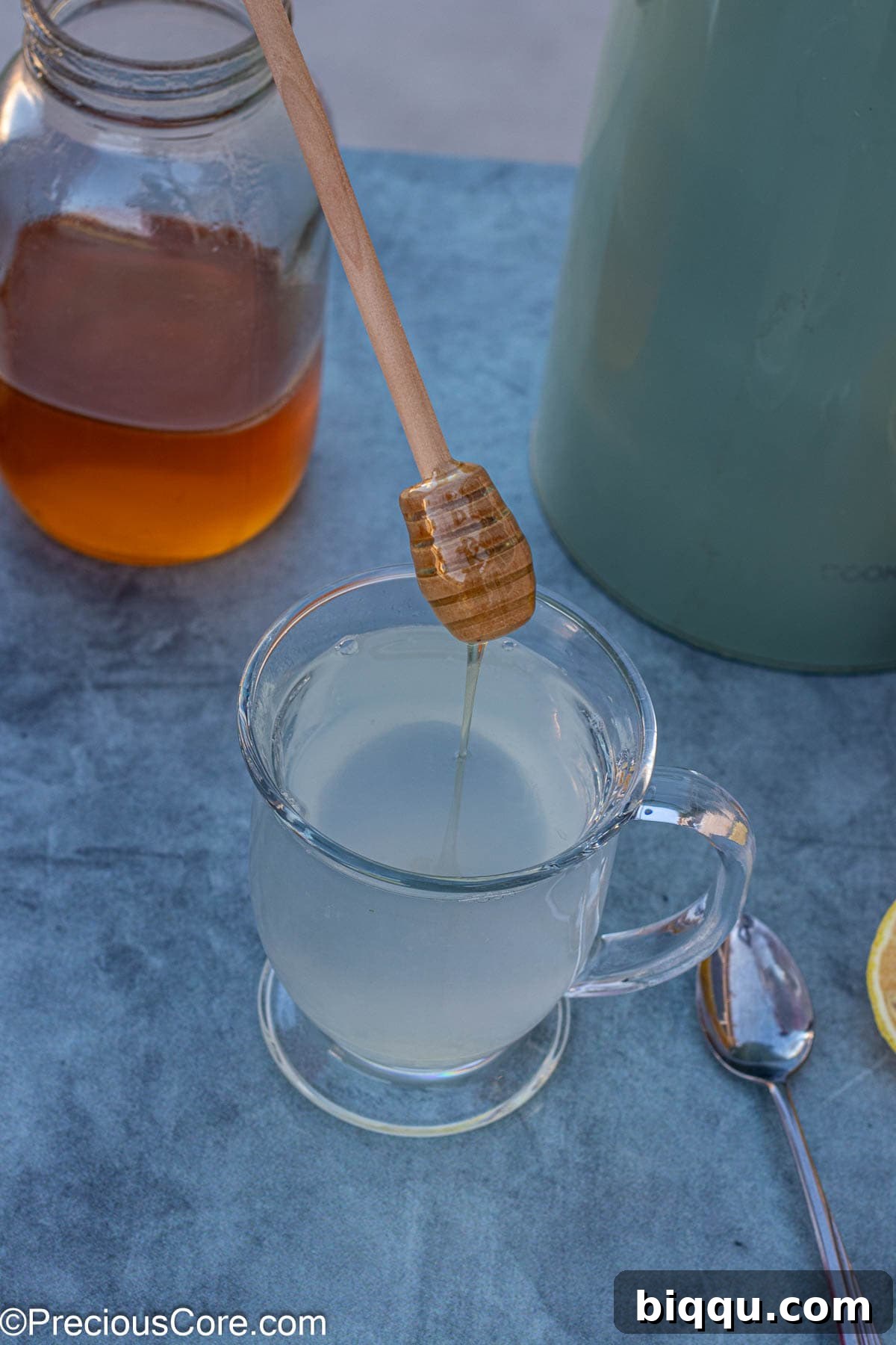 A stream of golden honey being poured into a mug of hot lemon water, creating a visual blend of the two ingredients.