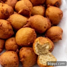 A platter brimming with golden-brown Banana Fritters, with one cut open to reveal its fluffy internal texture.
