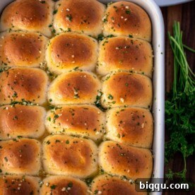 A full baking dish of golden-brown dinner rolls, generously brushed with aromatic garlic butter, ready to be served.