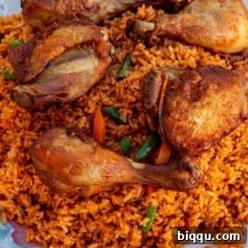 A serving platter piled high with vibrant Jollof Rice, topped with perfectly cooked chicken thighs and drumsticks, ready to be enjoyed.