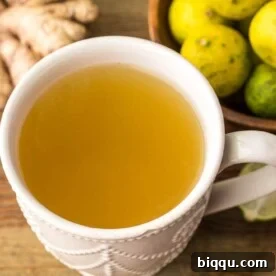 A warm mug of fresh ginger drink, elegantly presented with slices of ginger and key limes on the side, emphasizing its natural ingredients.