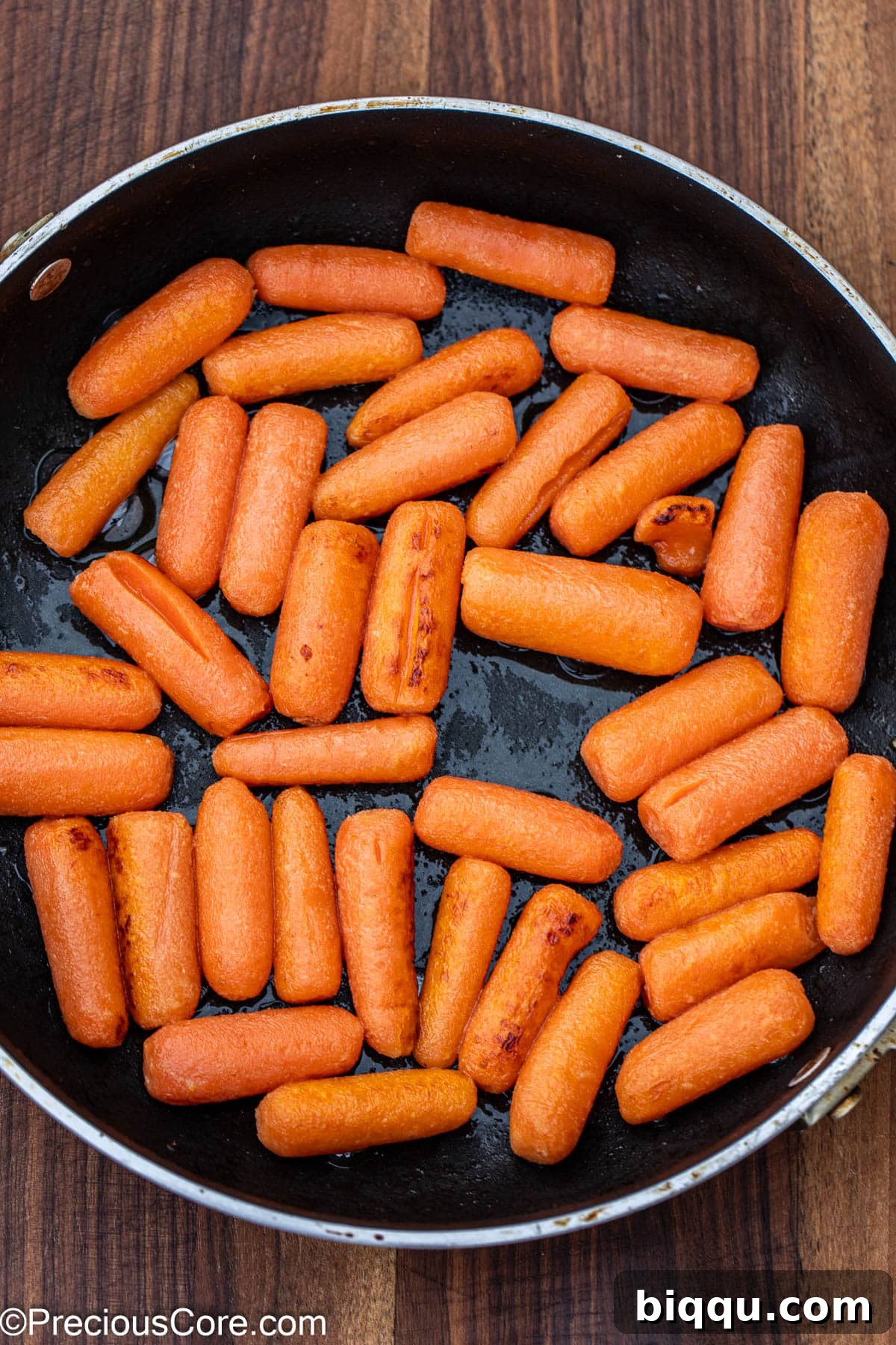 Carrots cooking in melted butter in a skillet, beginning to soften and brown.