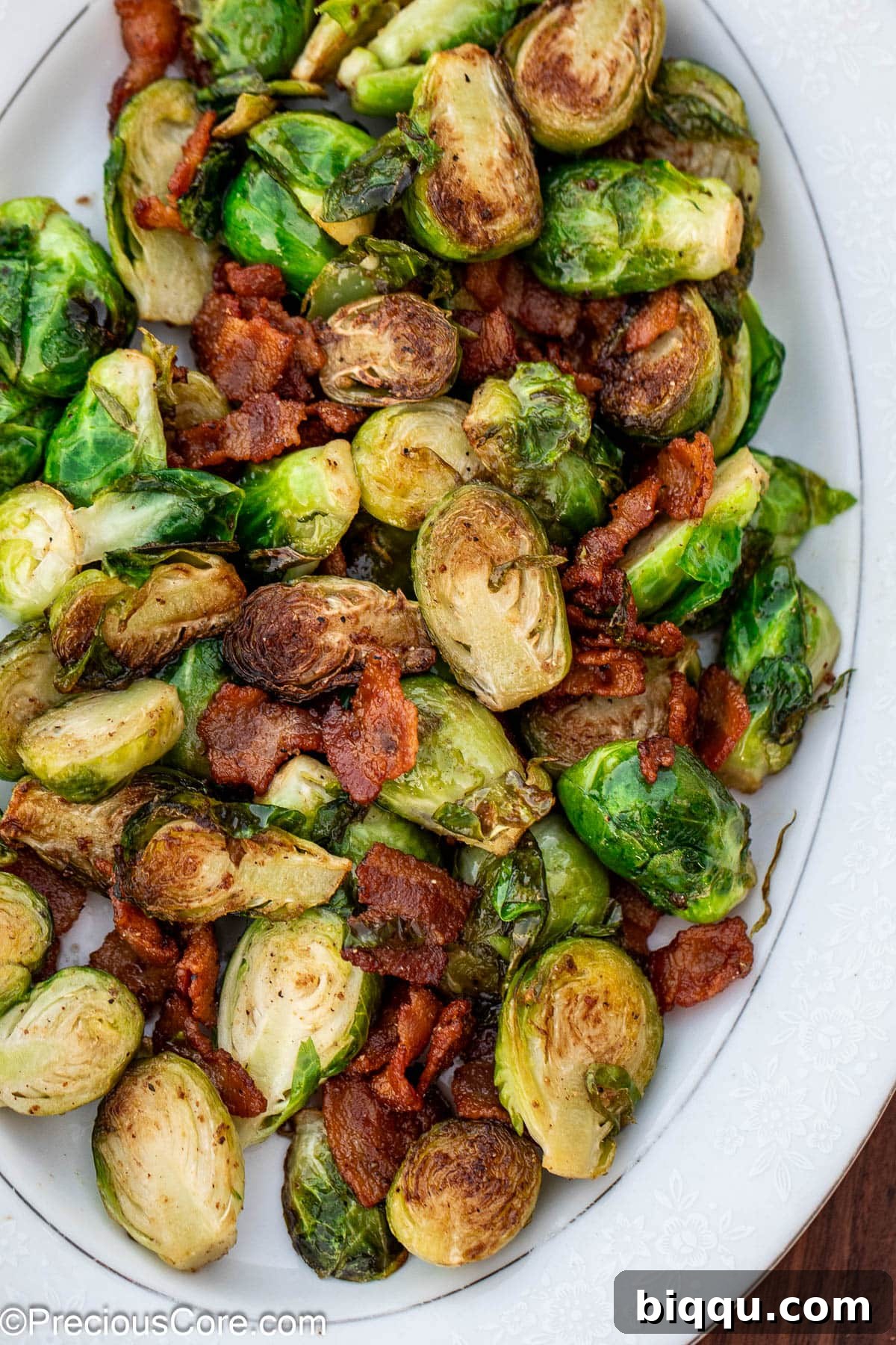 Cooked bacon and Brussels sprouts on a white serving plate.