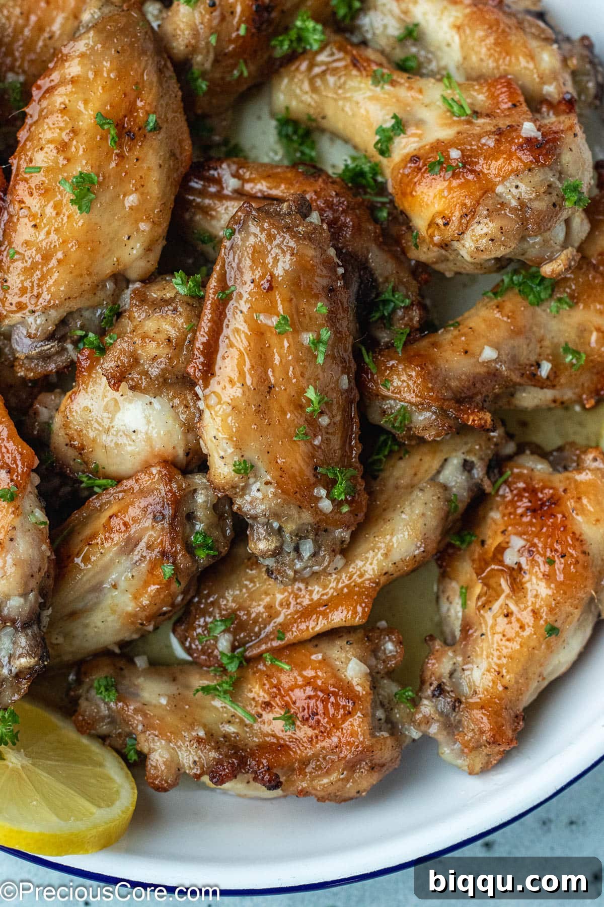 A bowl overflowing with golden-brown chicken wings, generously coated in shimmering garlic butter sauce pooled at the bottom.